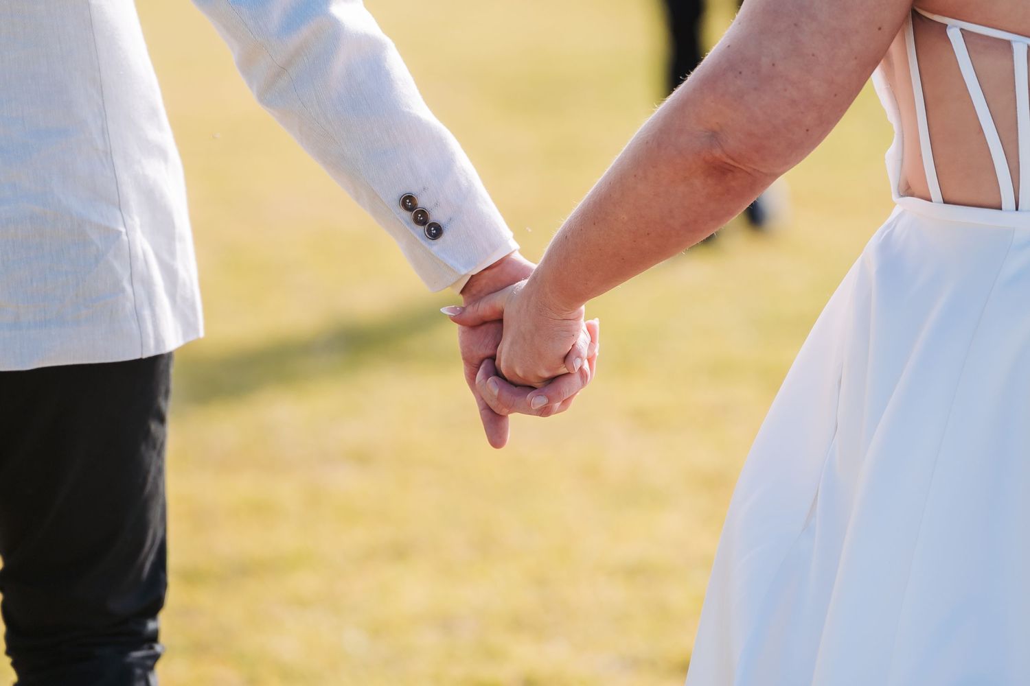 Close-up of newlyweds holding hands showing wedding attire details.