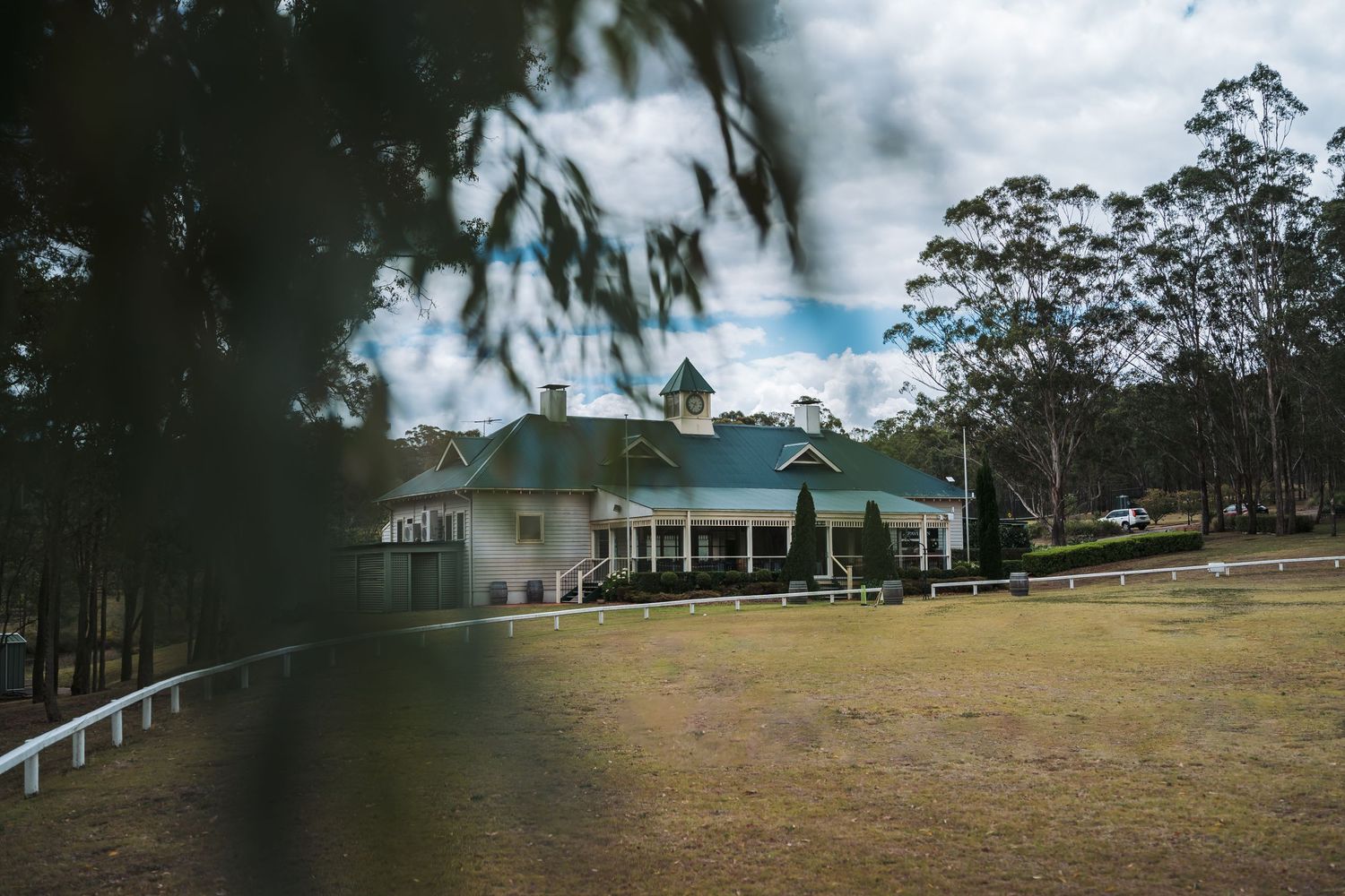 A white country house with a wraparound porch set against rolling hills and eucalyptus trees.