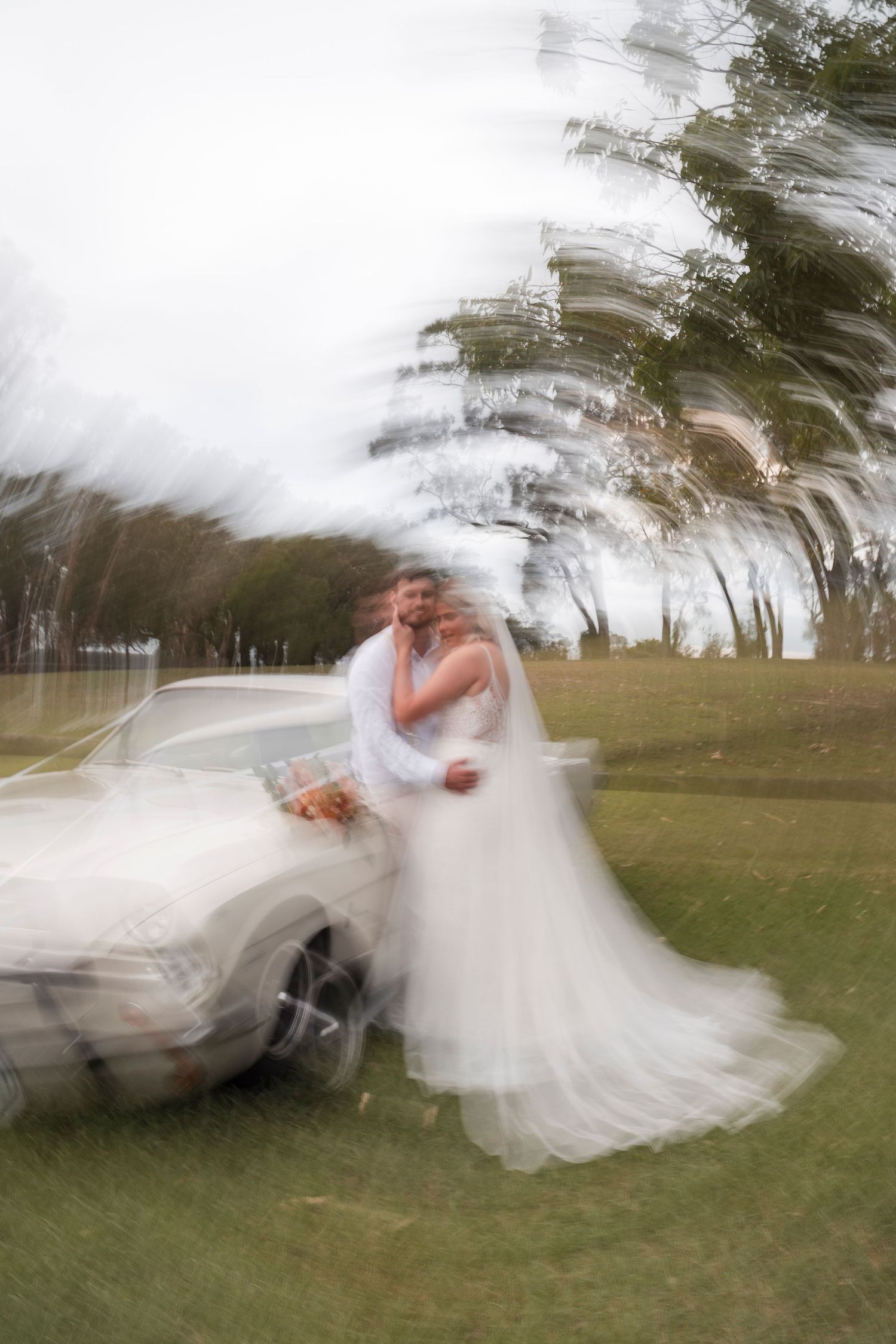 Artistic motion blur wedding photo with classic car and flowing dress.