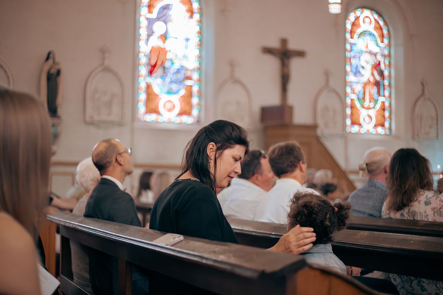 Woman bowing her head in prayer while seated in a church pew during a baptism service.