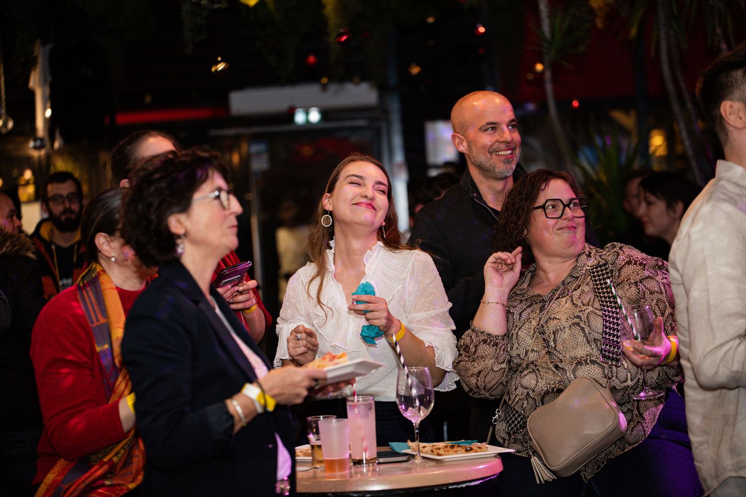 Group of people laughing and enjoying drinks at a festive indoor party event.