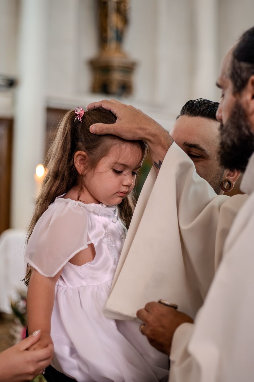 Priest placing hand on young girl's head during baptism ceremony in church.
