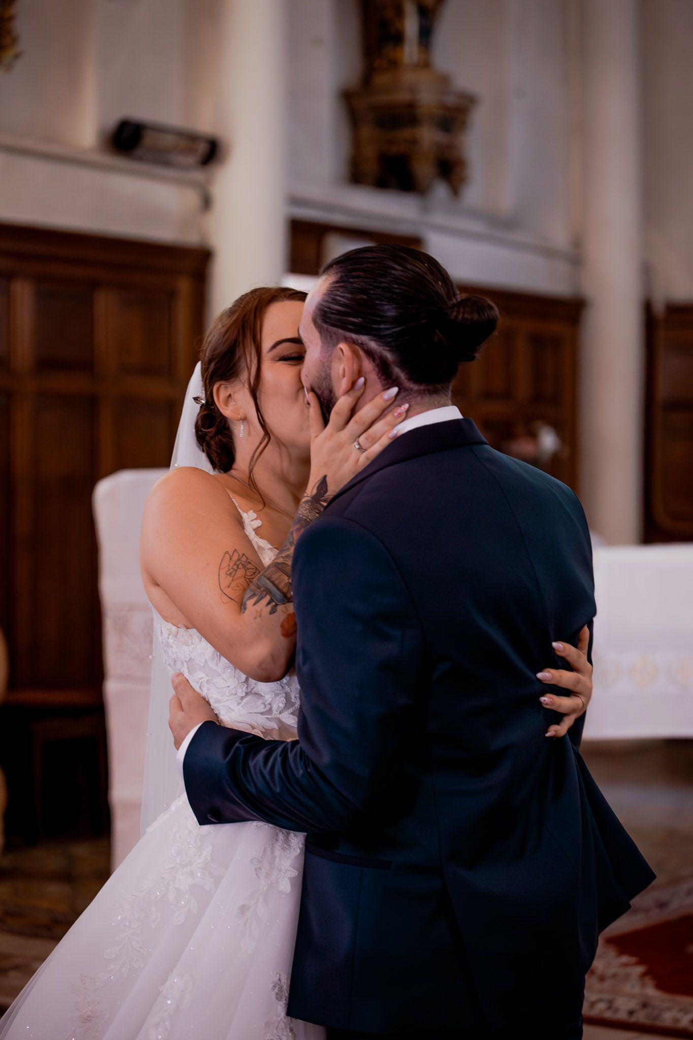 Bride and groom sharing a passionate kiss during their church wedding ceremony, with the bride in a lace gown.