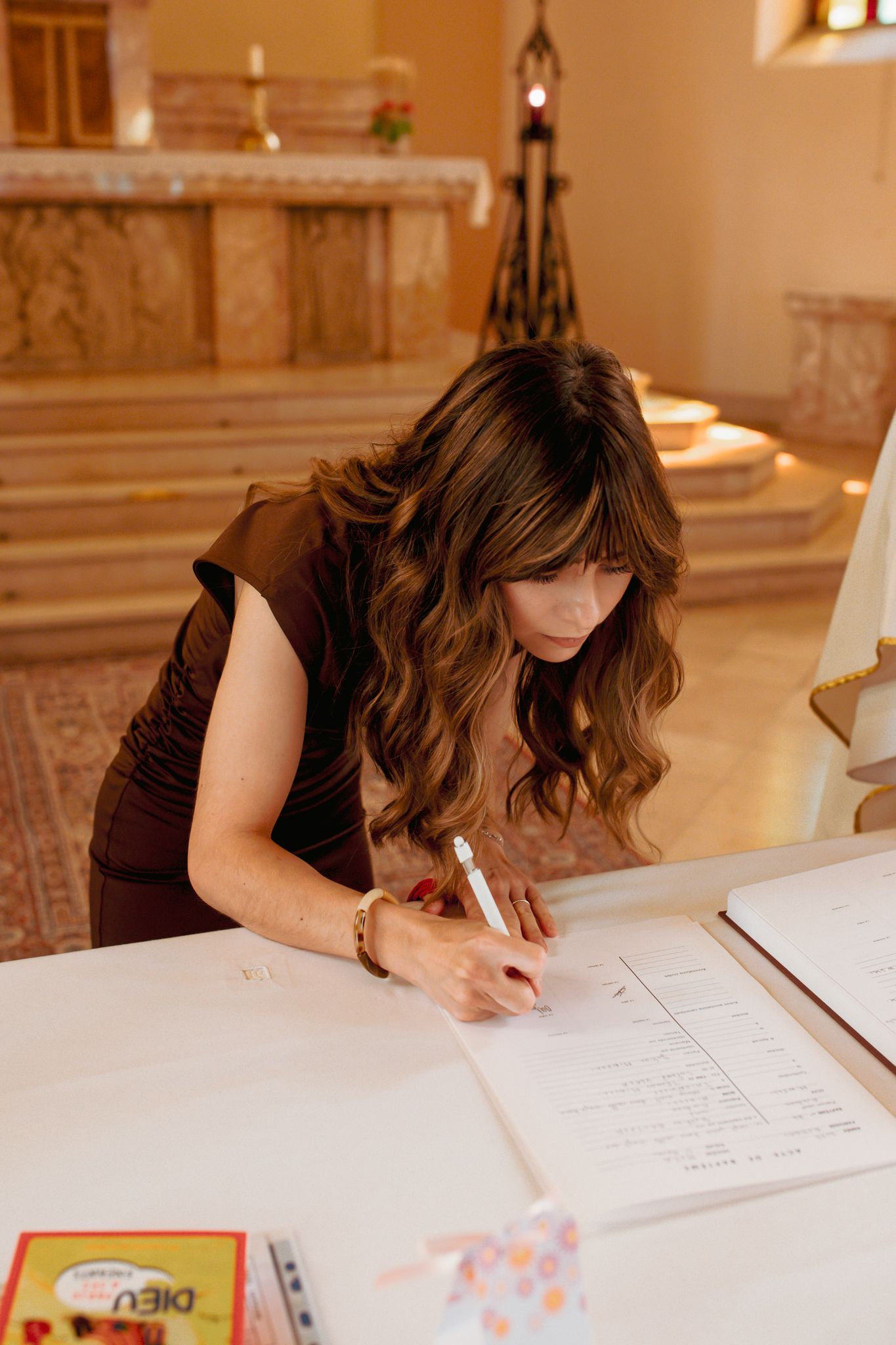 Woman with wavy brown hair signing a baptism register inside a church.