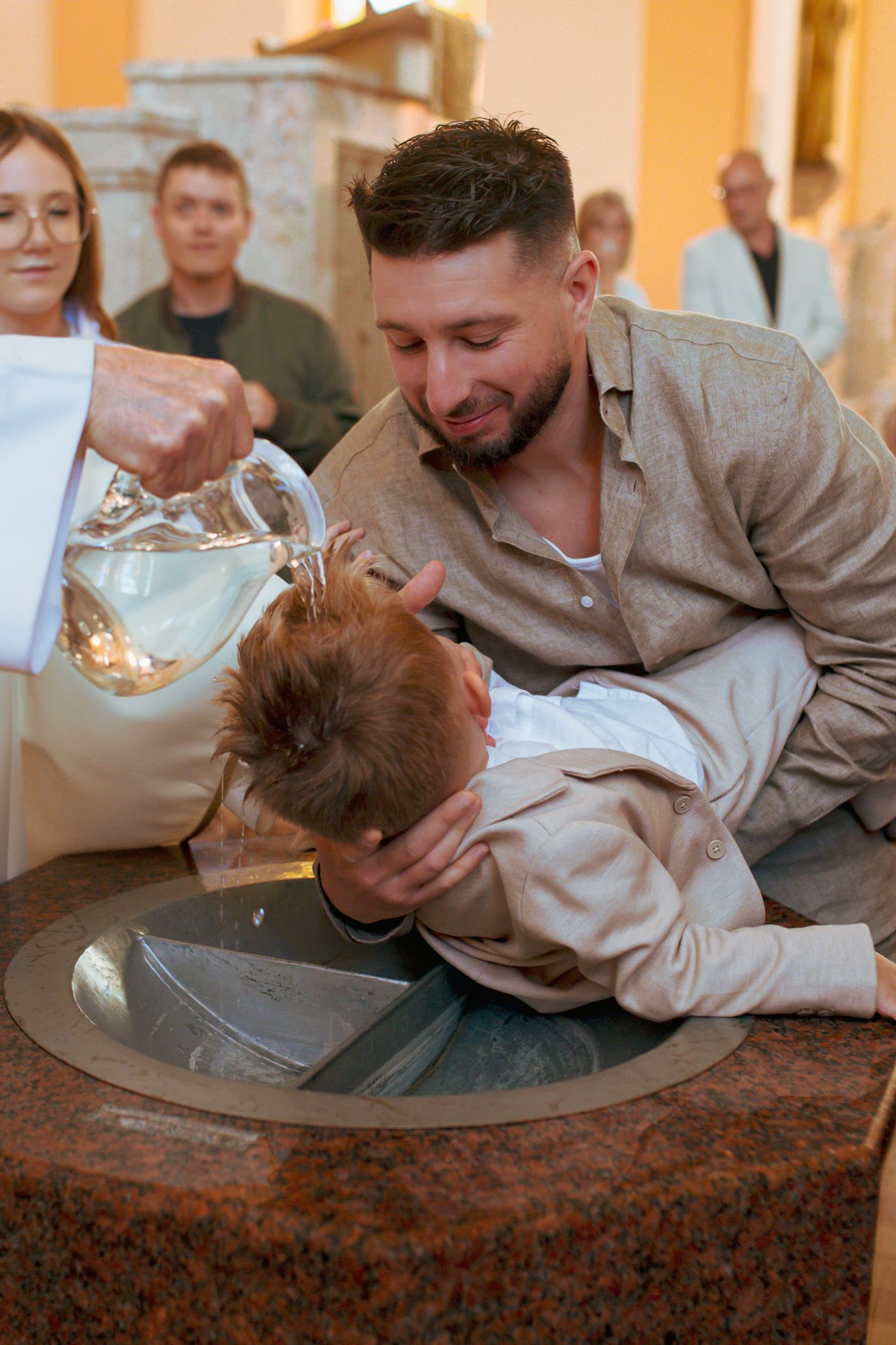 Priest pours holy water over child's head during a baptism ceremony in church.