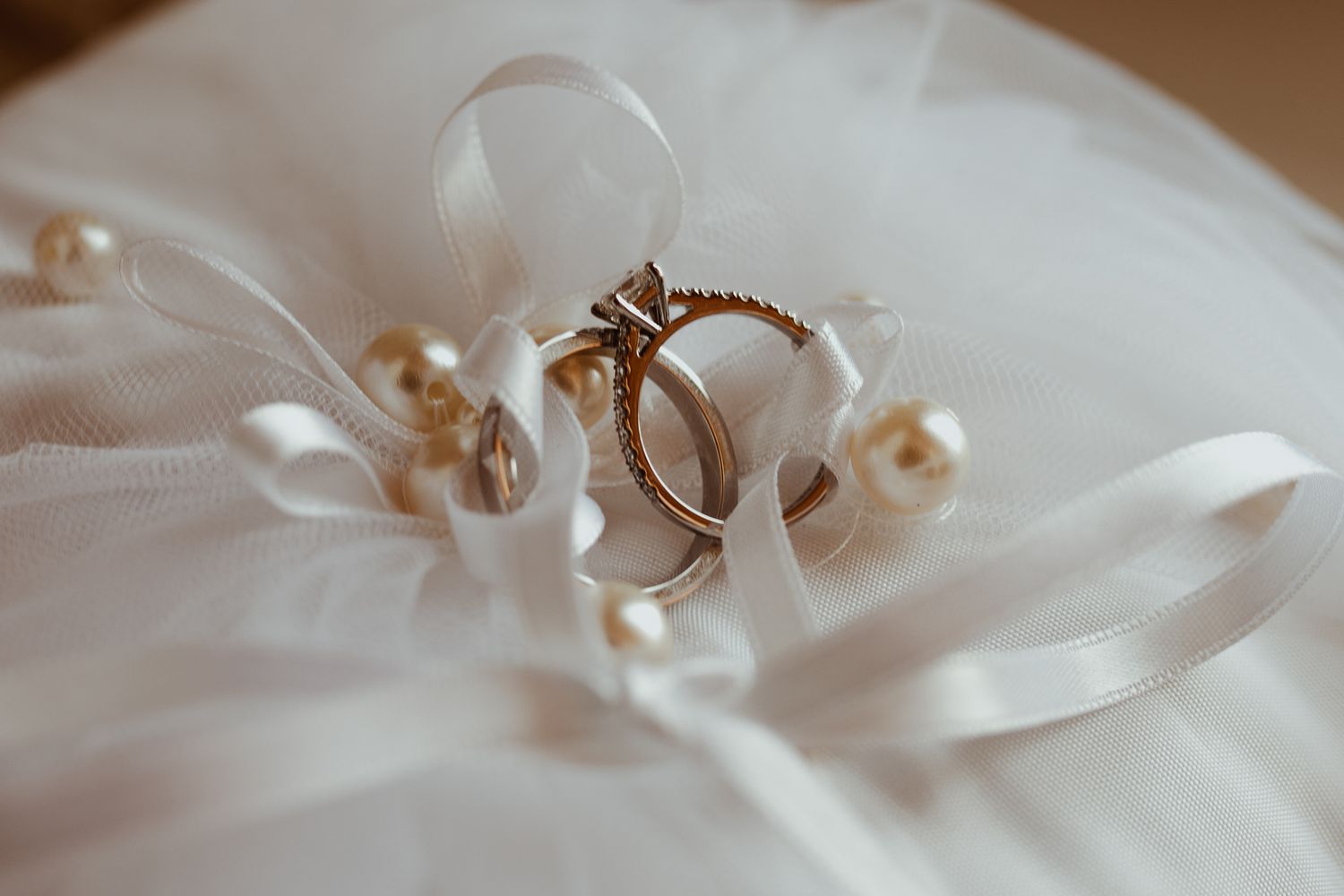 Gold wedding rings and engagement ring on white tulle fabric with pearl decorations.