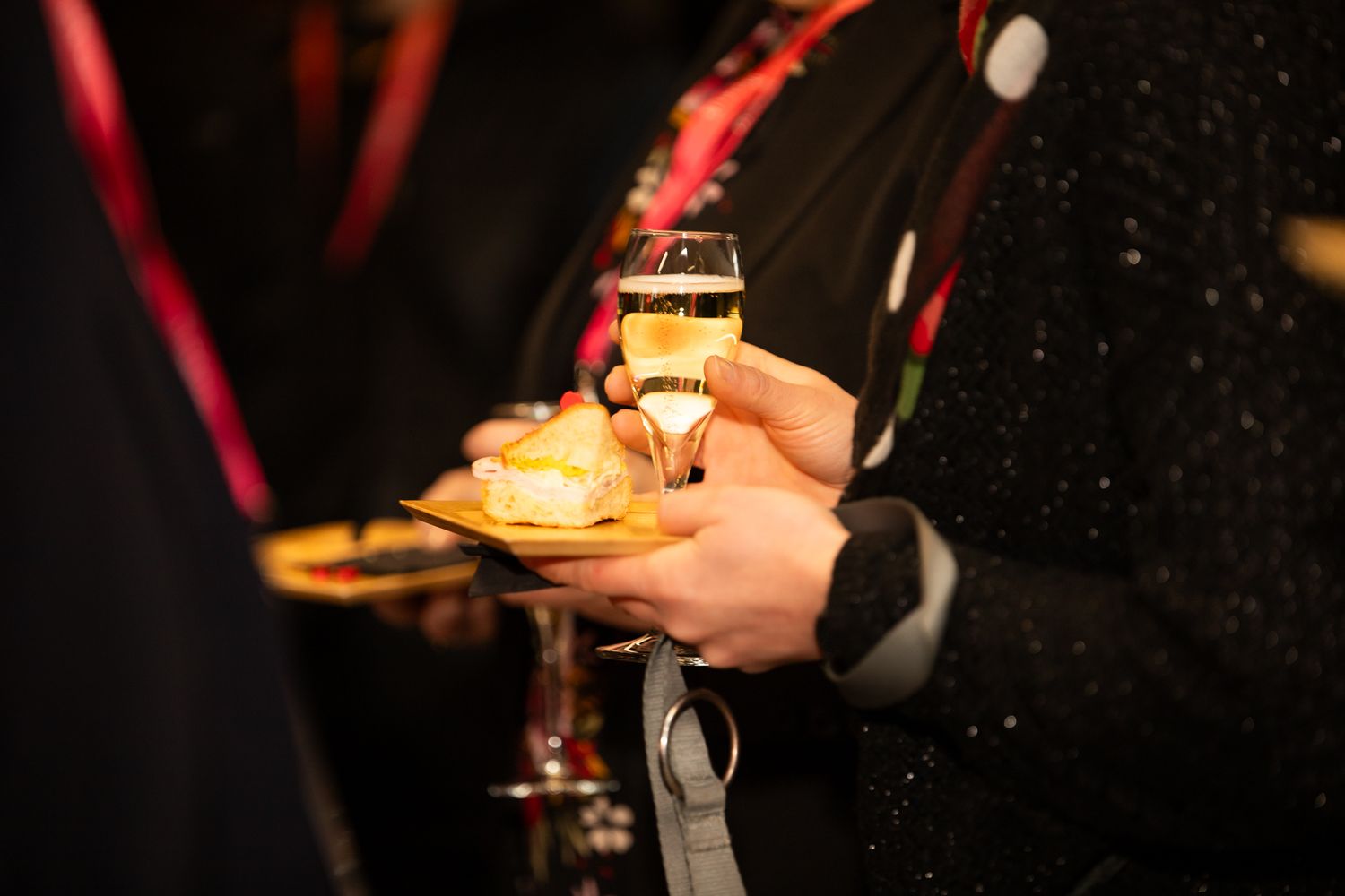 Person holding champagne glass and canape at an elegant networking reception event.