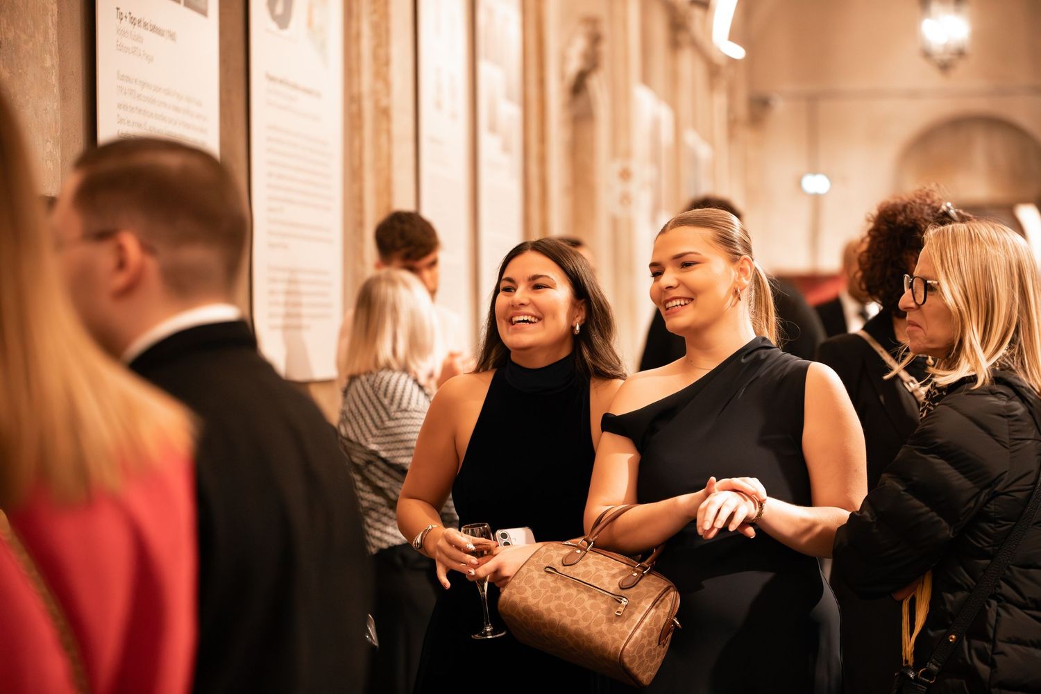 Two women in black dresses smiling and chatting at a formal event.
