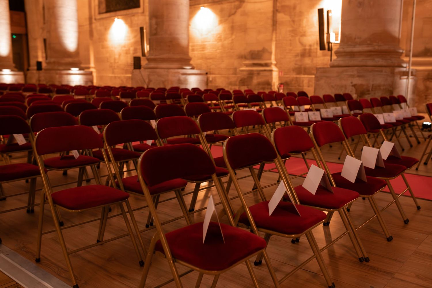 Rows of empty red folding chairs arranged in ornate hall for formal ceremony.