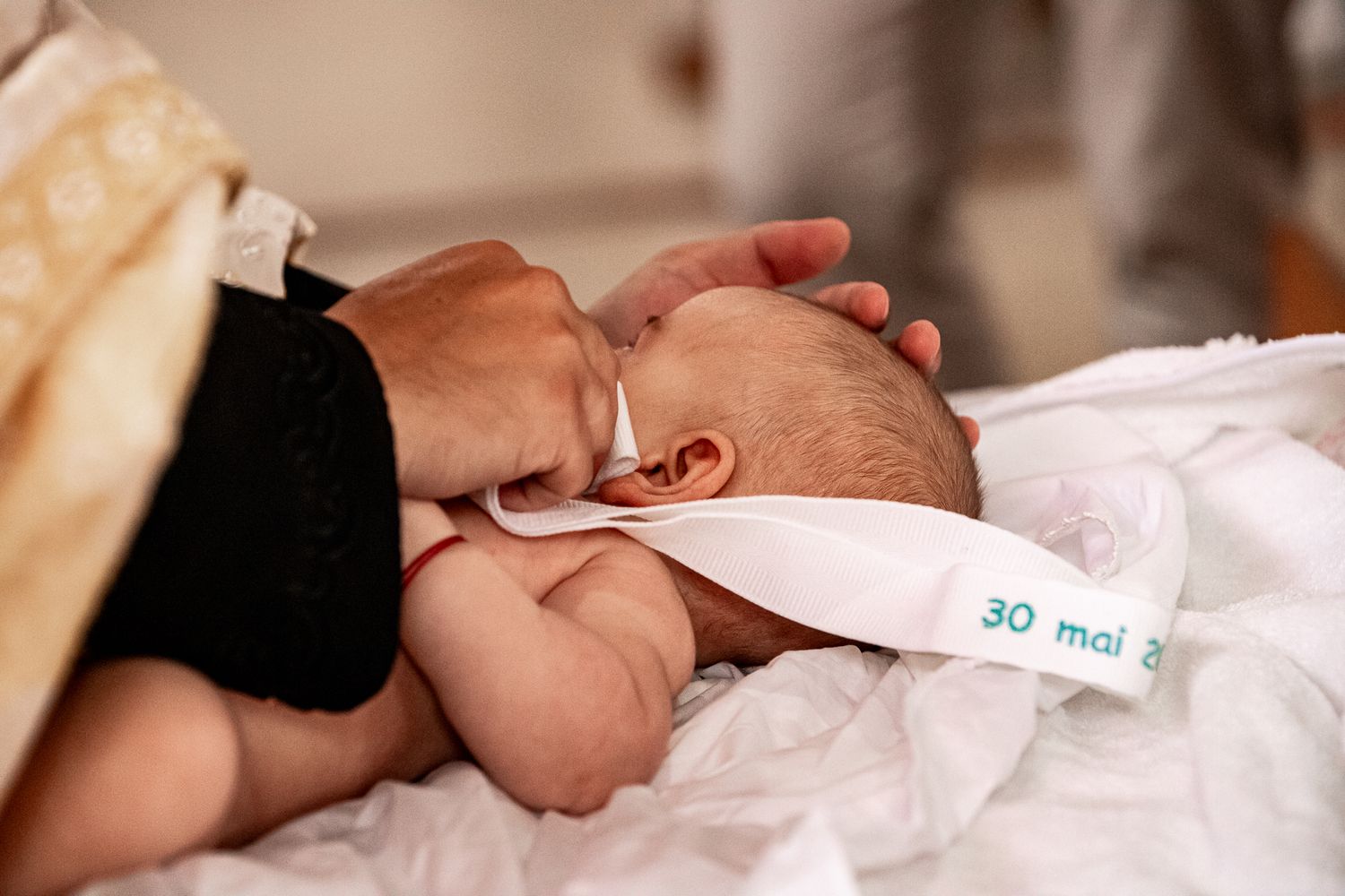 Priest anointing a newborn baby wrapped in white cloth during a baptism ceremony.