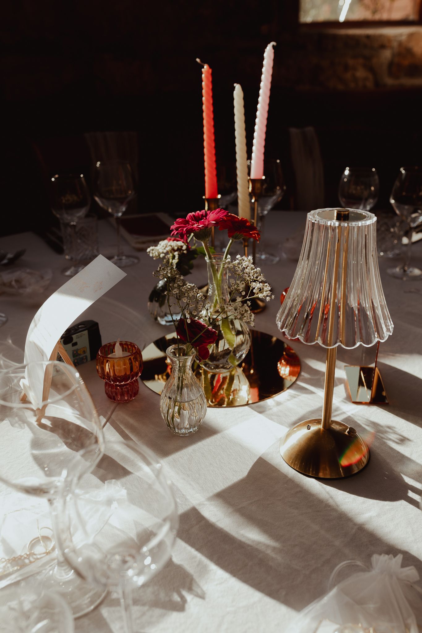 Wedding reception table with candles, flowers, and a glass lamp casting warm shadows.
