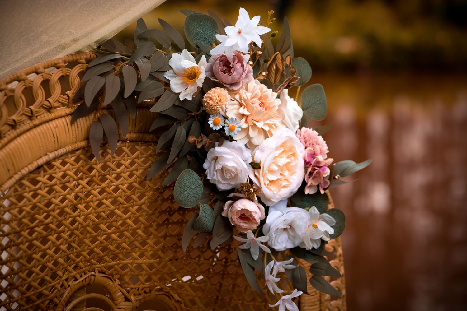 Elegant wedding floral arrangement with peach roses and eucalyptus on a wicker chair.