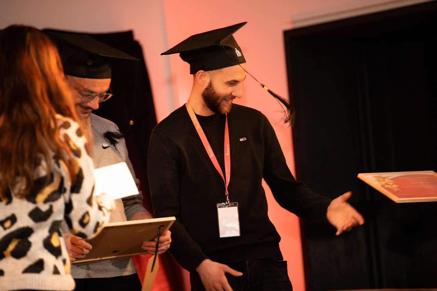 Two people wearing graduation caps on stage during a conference ceremony with a diploma.