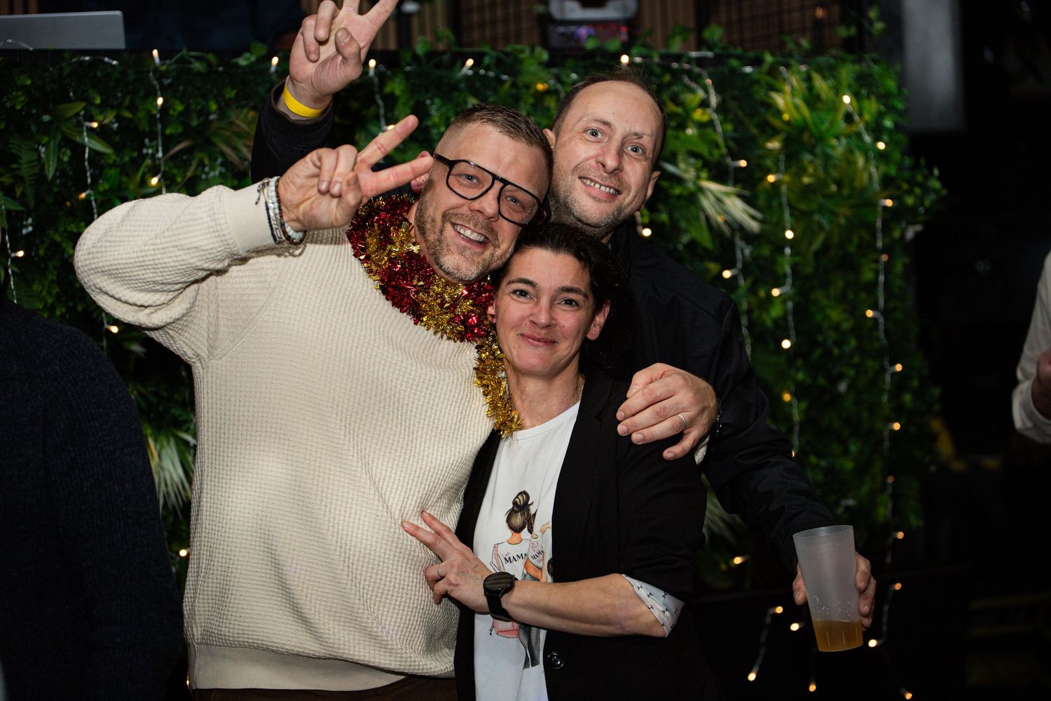 Three friends posing together and smiling at a festive holiday party celebration.