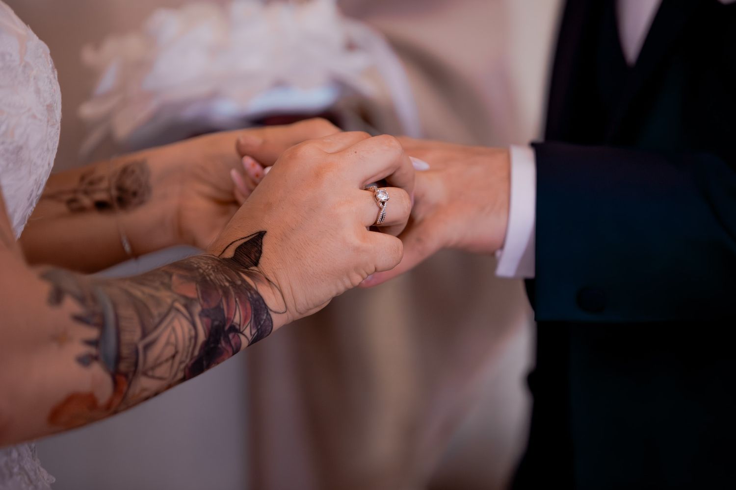 Close-up of couple exchanging wedding rings, bride with tattoed arm wearing elegant ring during ceremony.