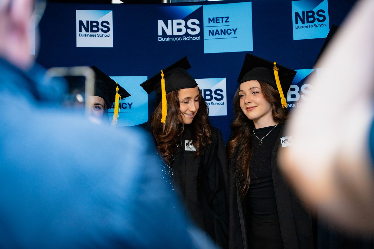 Two NBS graduates in caps and gowns posing for photo at ceremony.