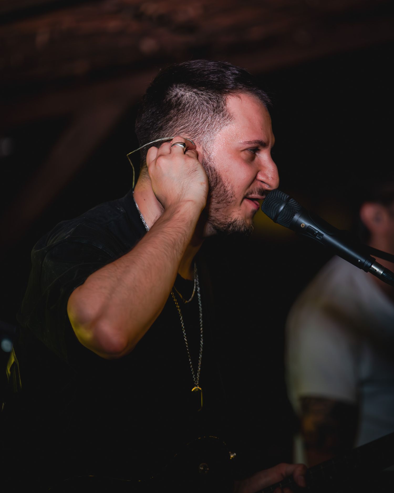 Male singer performing on stage adjusting in-ear monitor at a dimly lit music venue.