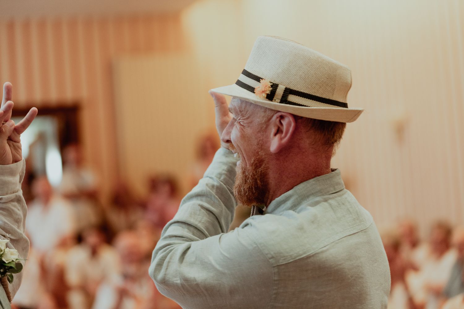 Bearded man wearing a straw panama hat speaks at an indoor event, gesturing with his hand.