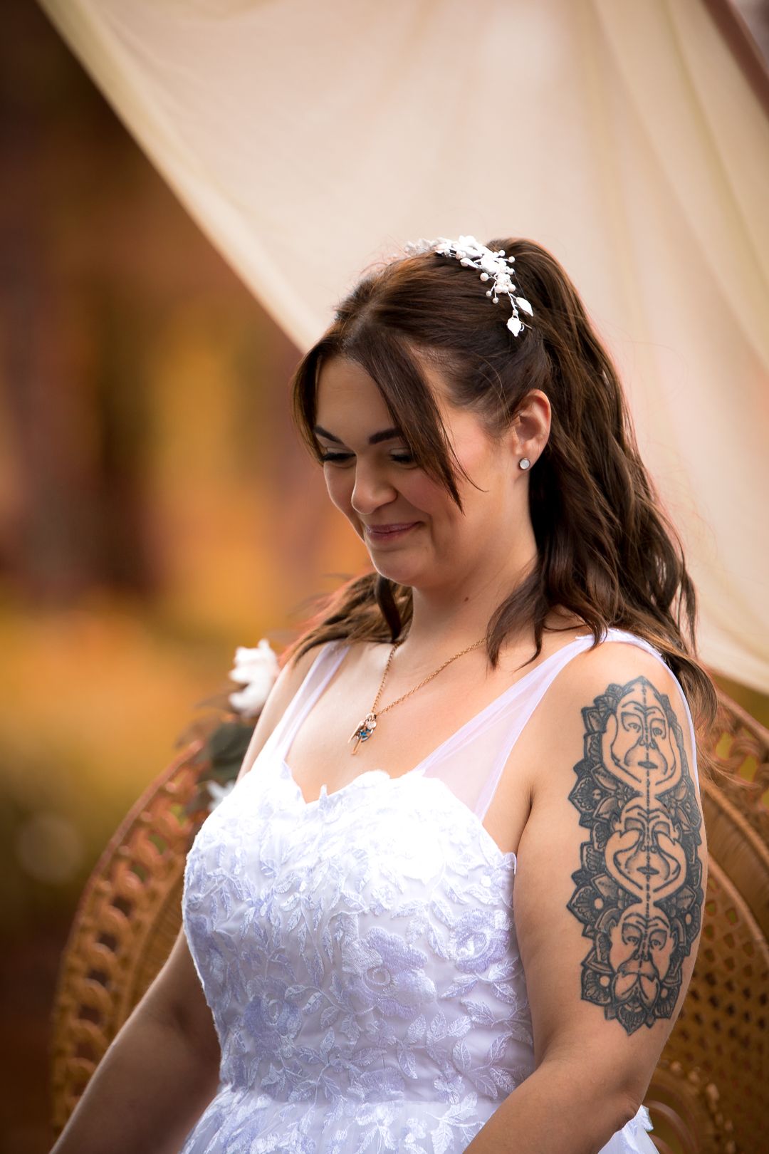 Bride in white dress with arm tattoo and floral hair accessory smiling softly.