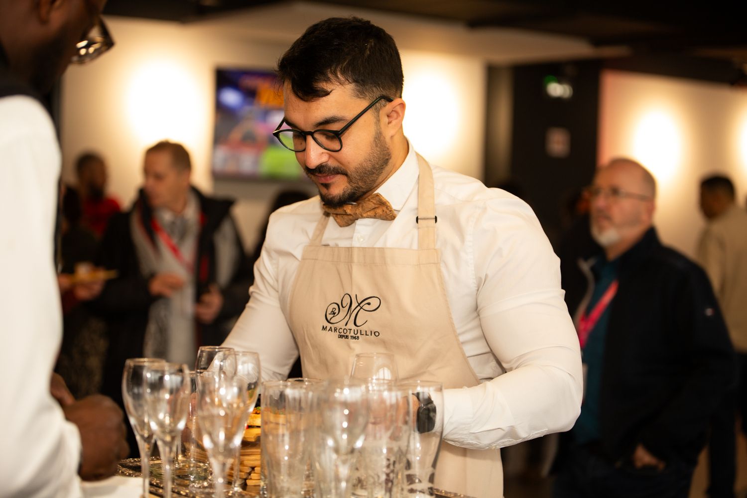 Barman en nœud papillon et tablier arrangeant des verres lors d'une élégante réception d'événement.