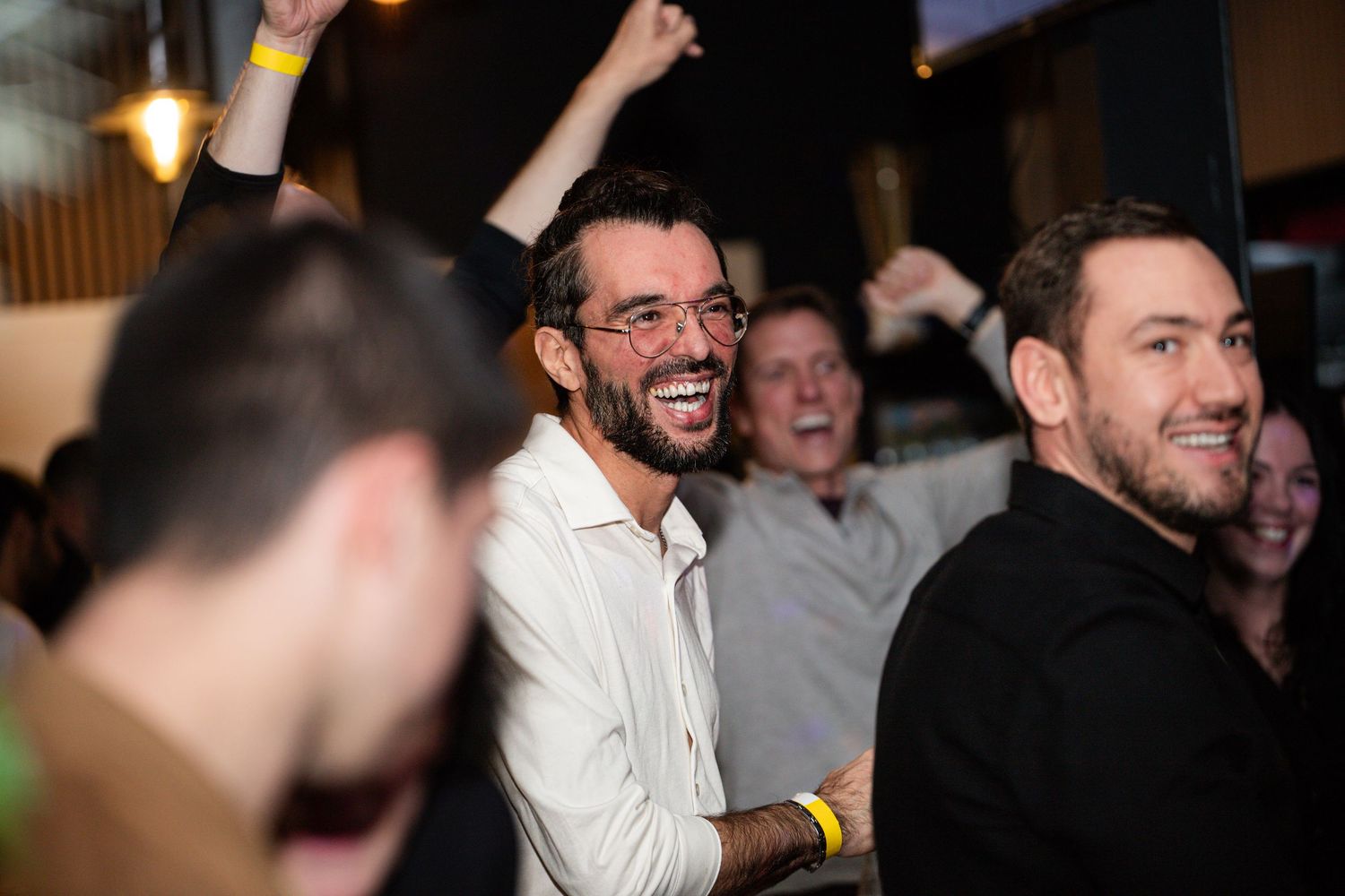 Excited man in white shirt laughing with friends at a lively social gathering.