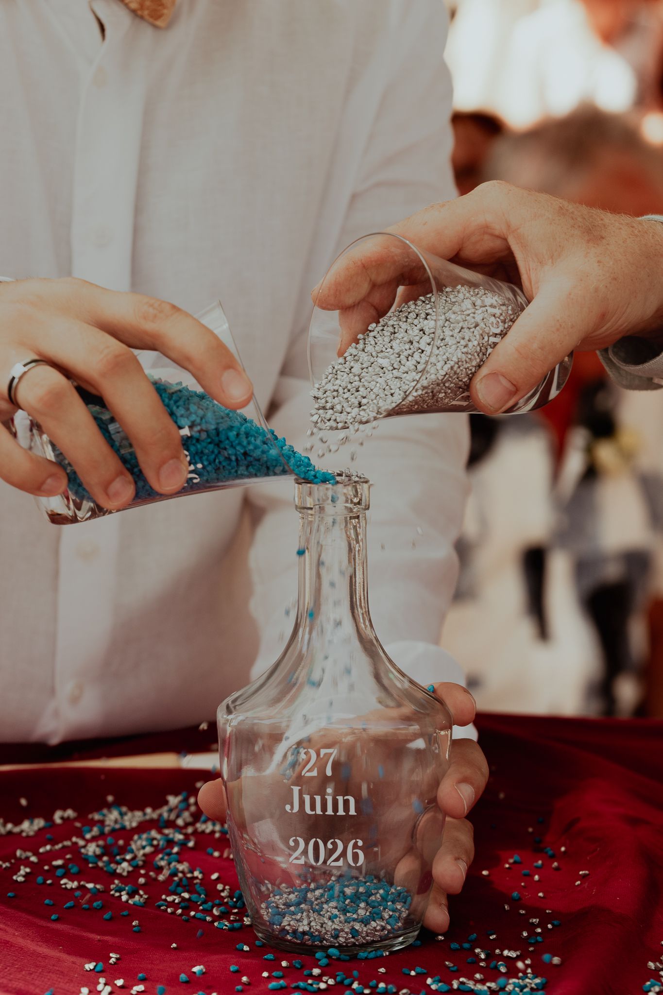 Two people pouring colored sand into a dated ceremony unity bottle on June 27 2026.