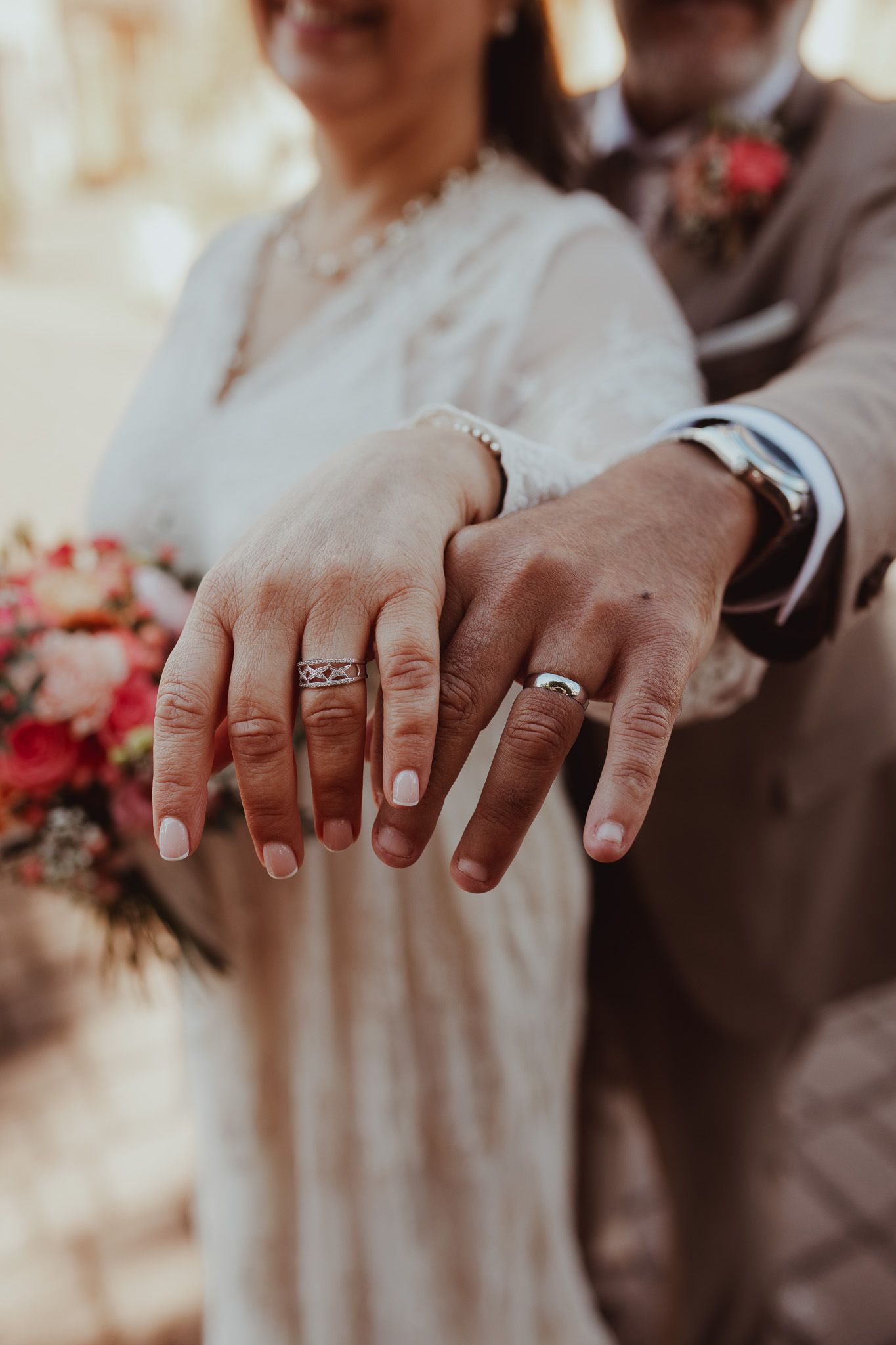 Newlywed couple displaying their wedding rings together, bride holding a colorful bouquet.