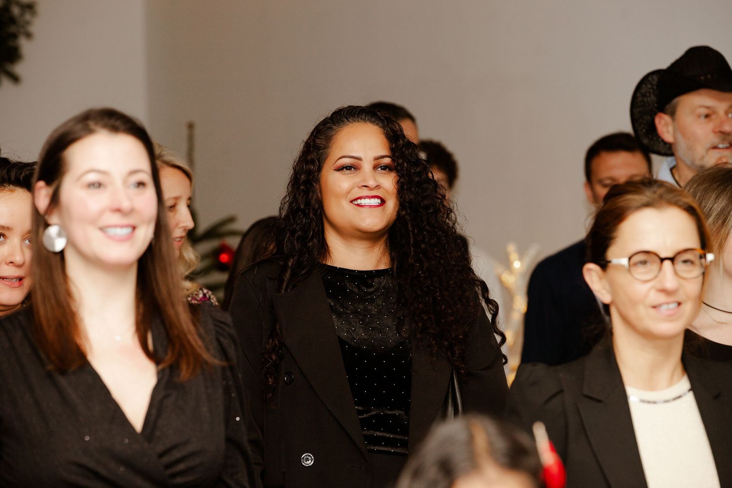 A diverse group of smiling women dressed in black at an indoor social gathering or corporate event.