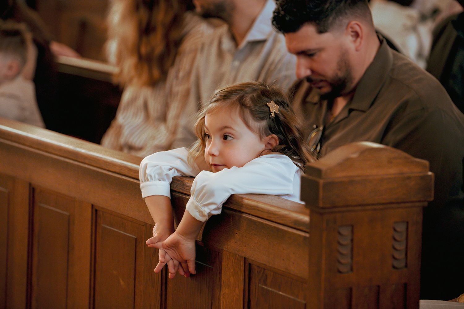 Young girl rests her chin on a wooden church pew during a religious ceremony.