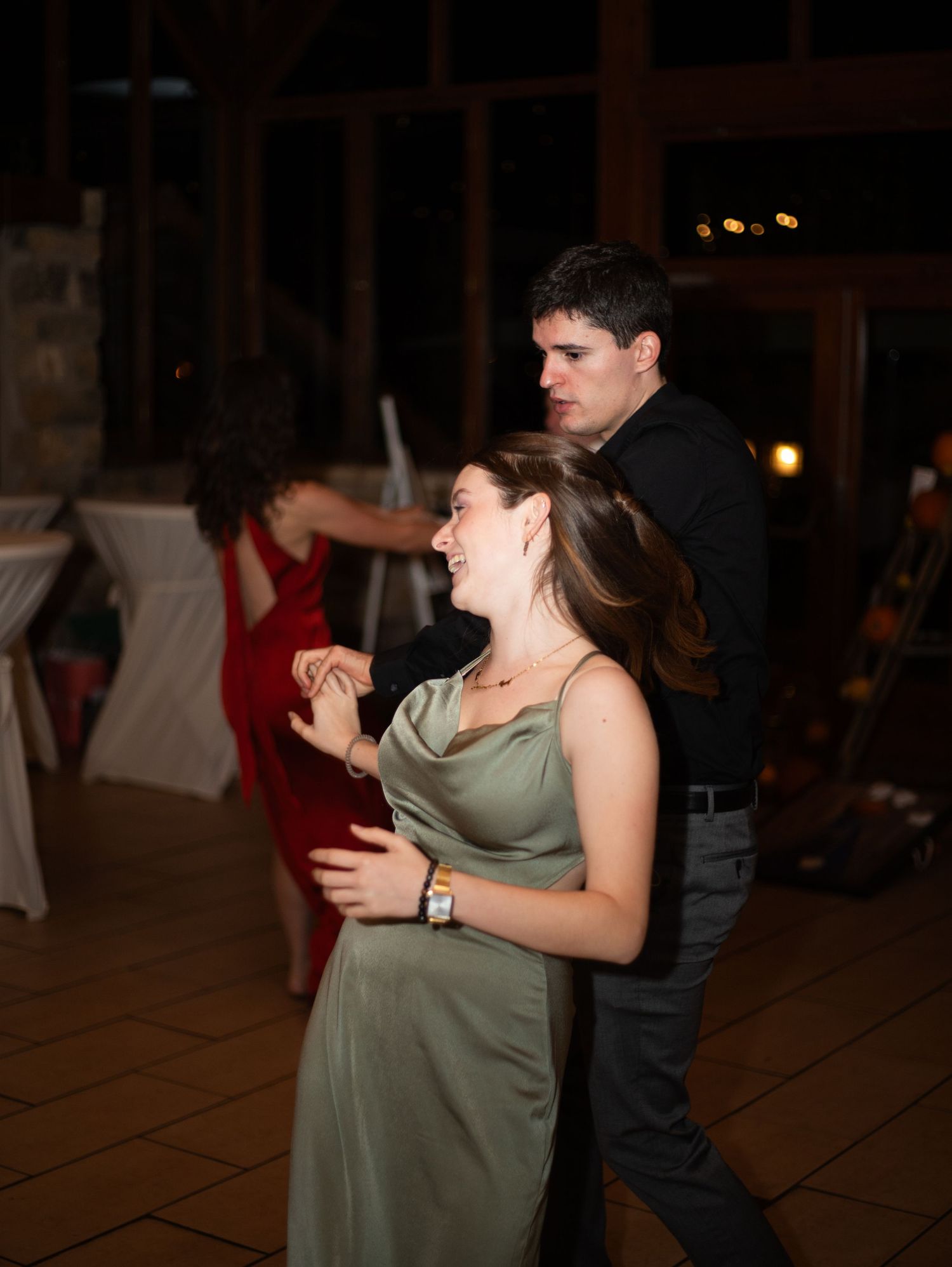 Couple dancing closely together at a wedding reception in a dimly lit venue with other guests in the background.