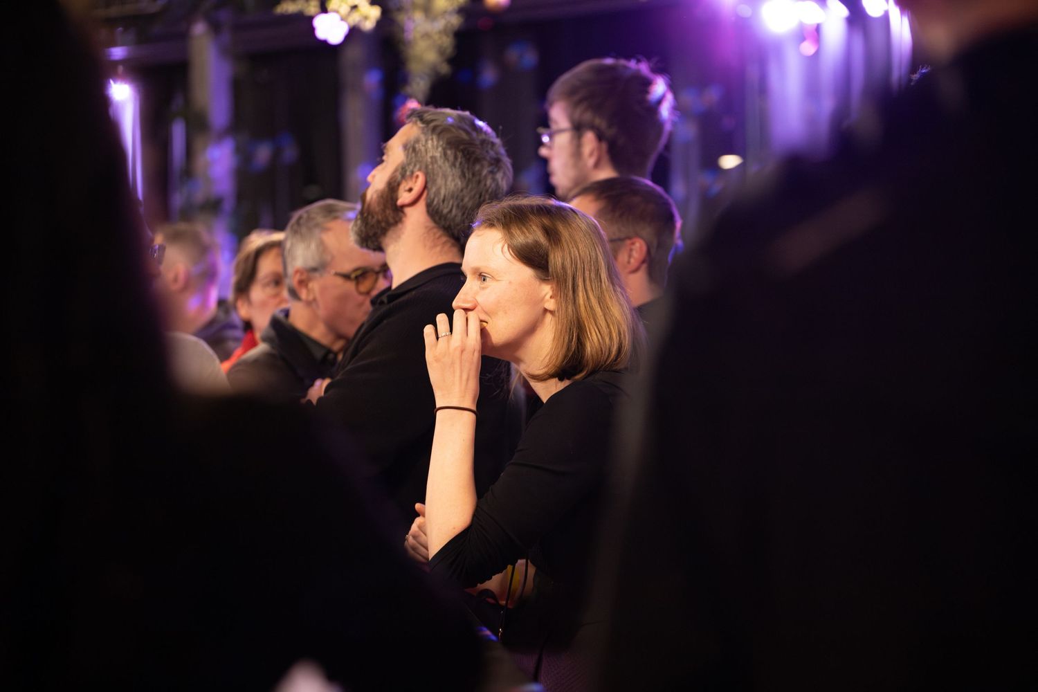 Crowd of attendees watching graduation ceremony in dimly lit venue.