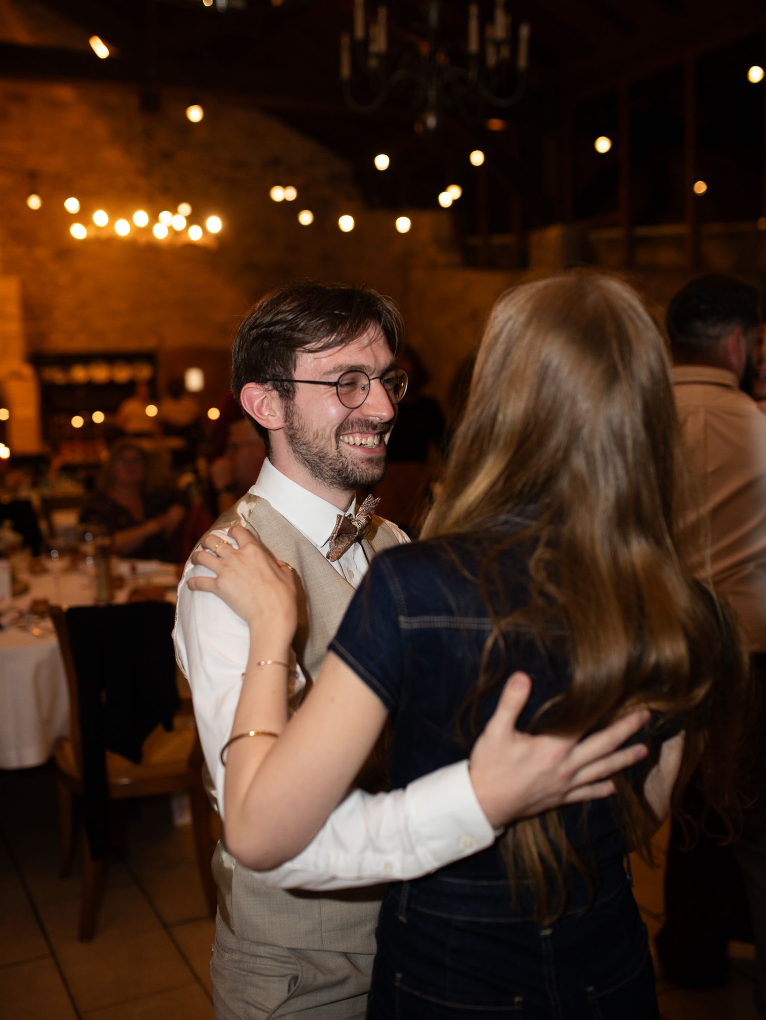 Smiling man with glasses and bow tie dancing with a woman at wedding reception.