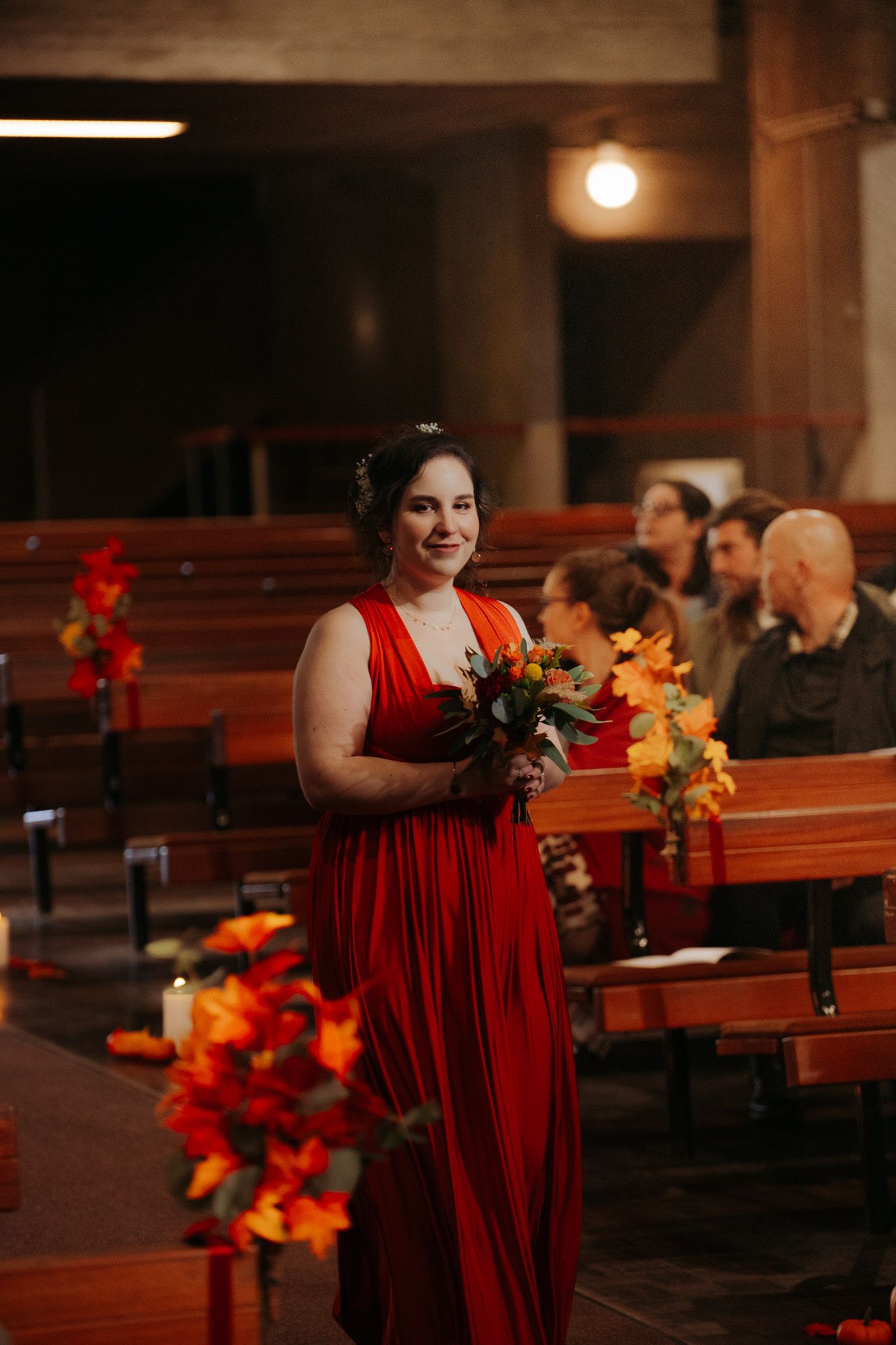 Demoiselle d'honneur en robe rouge portant un bouquet orange et rouge marchant dans l'allée de l'église au mariage.