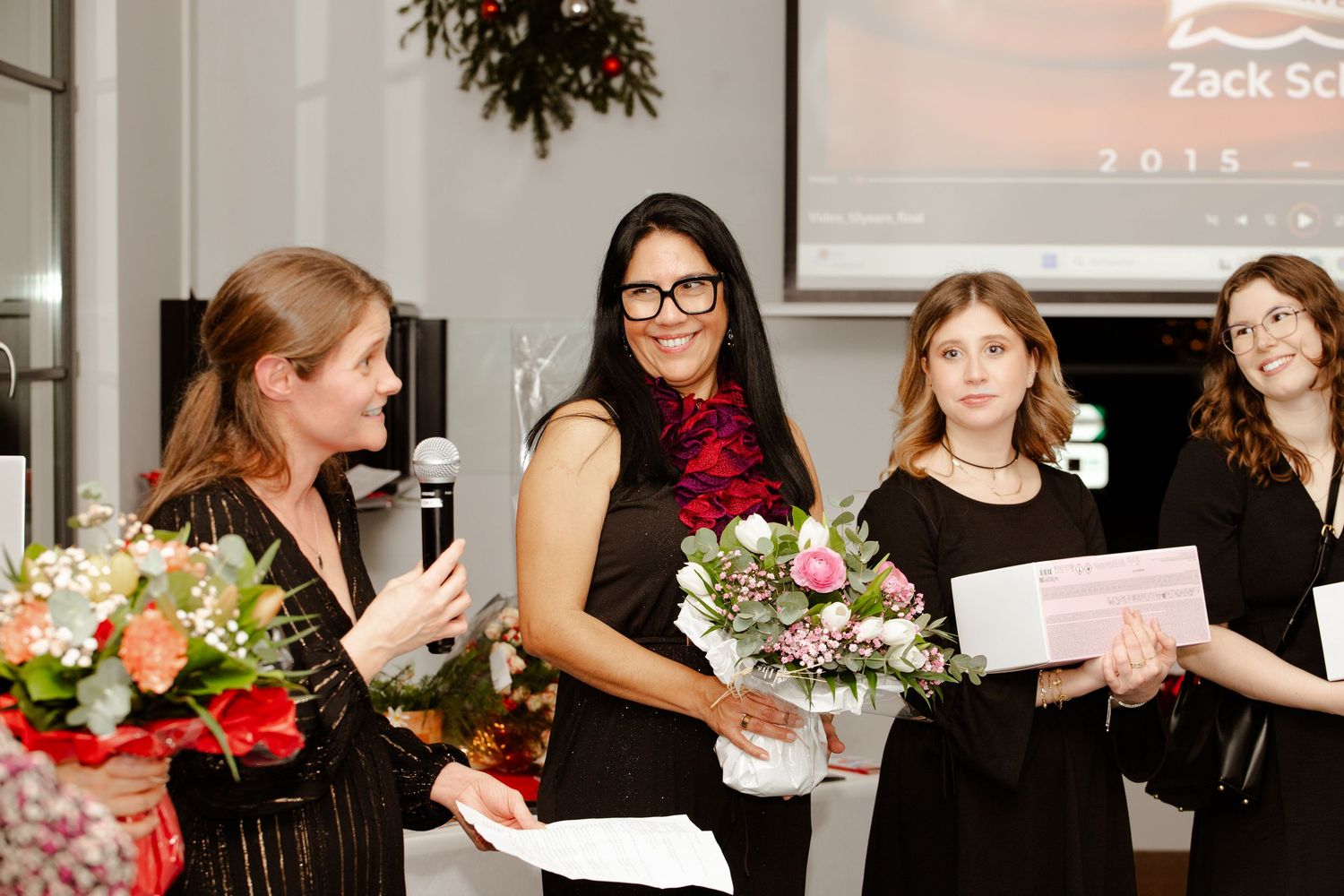 Women receive flower bouquets during an award presentation at a festive corporate event.