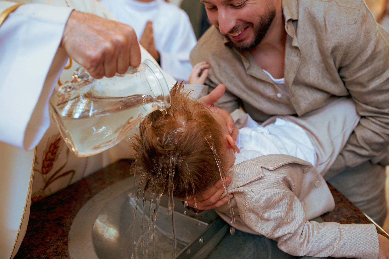 Priest pouring water over a baby's head during a Christian baptism ceremony.