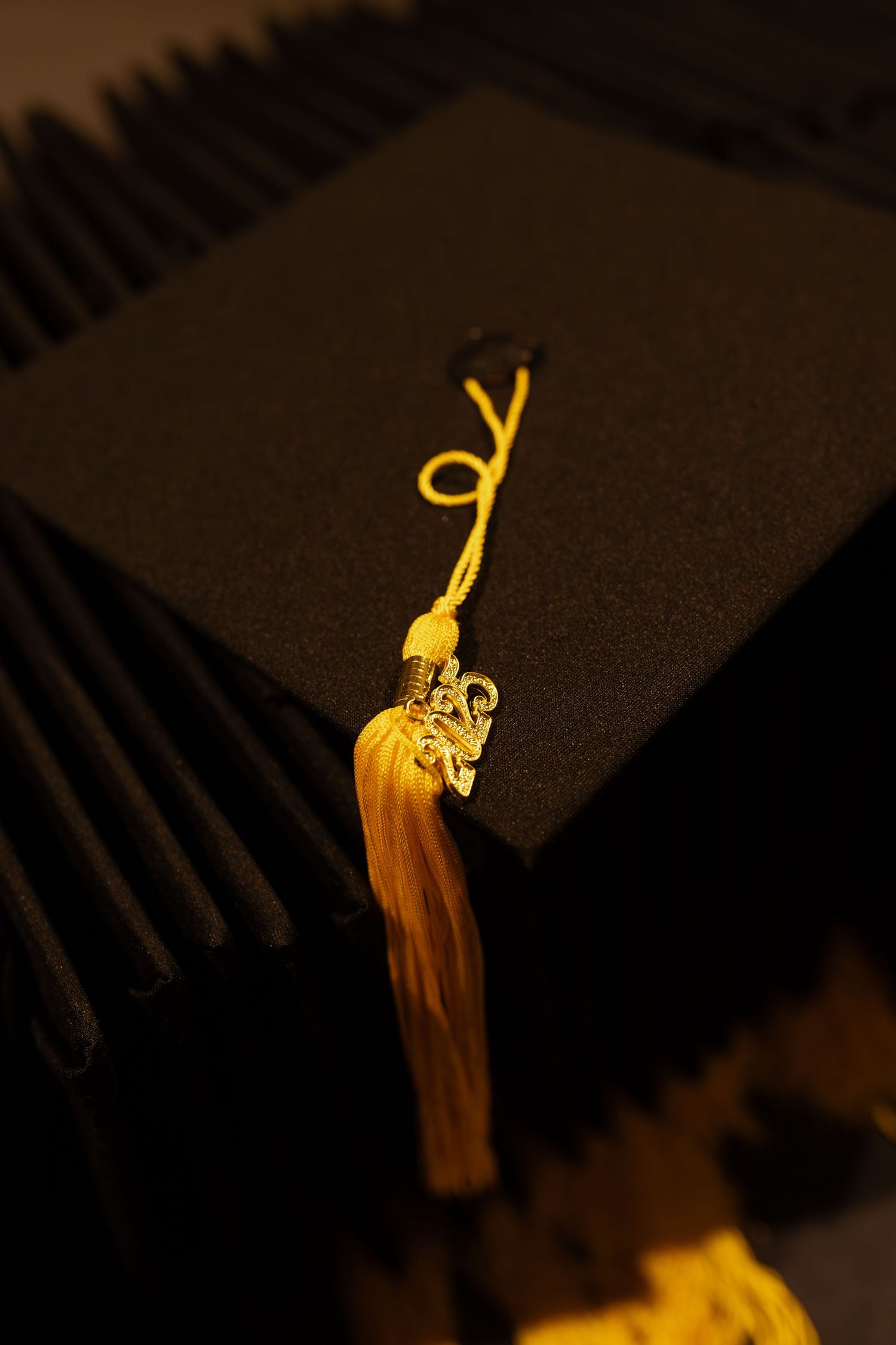 Close-up of black graduation cap with gold tassel and decorative charm.