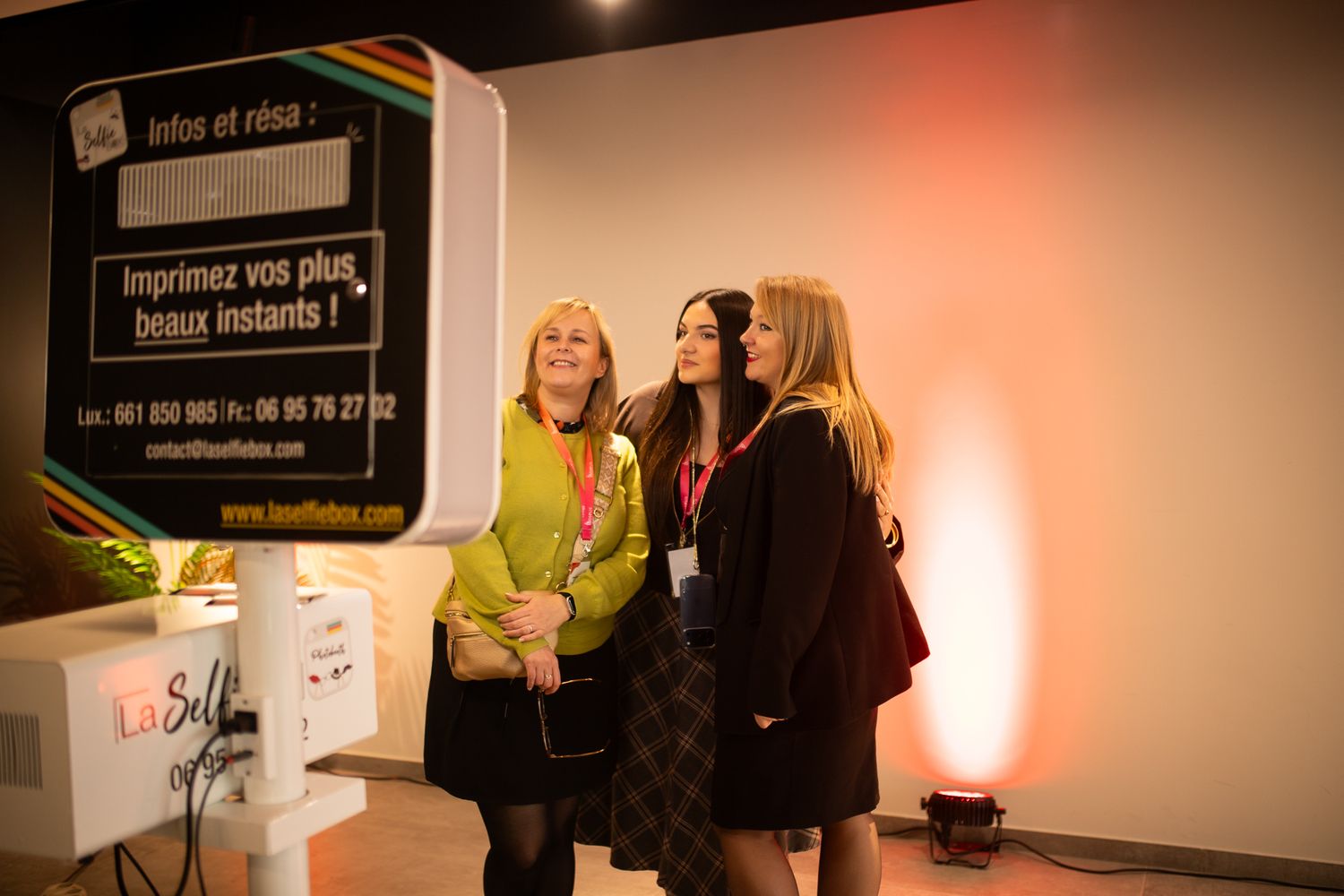 Trois femmes posant ensemble à un photomaton lors d'un événement intérieur.