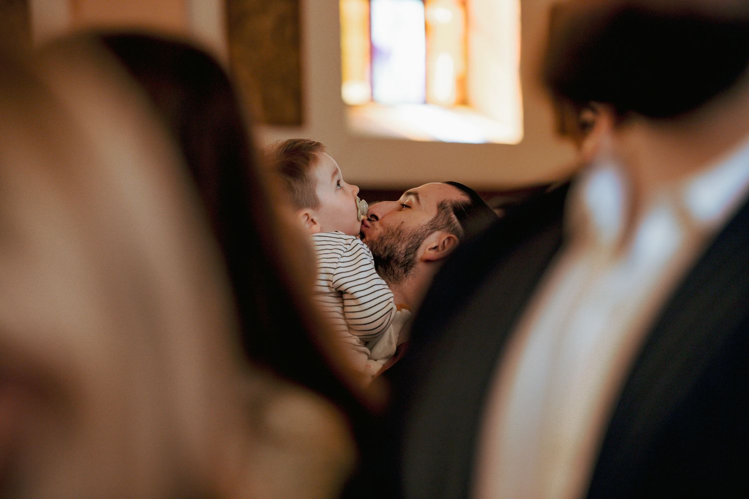 Father tenderly kissing his baby during a church baptism ceremony.
