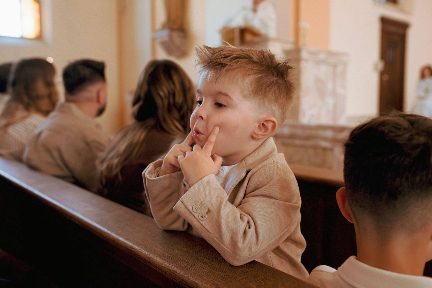 Young boy in beige suit sits praying in church pew during religious ceremony.