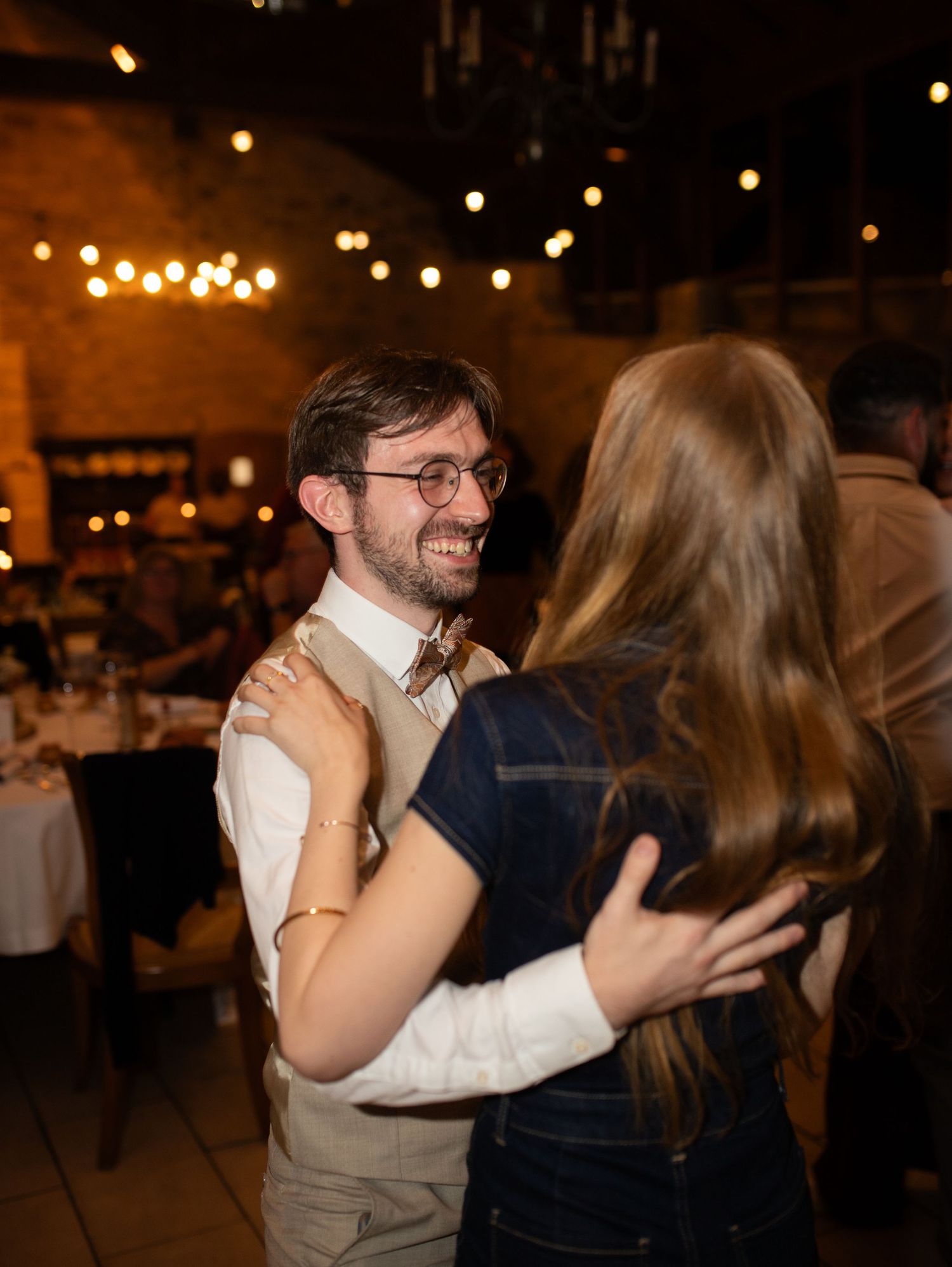 Couple dancing together at a warmly lit wedding reception venue with string lights overhead.