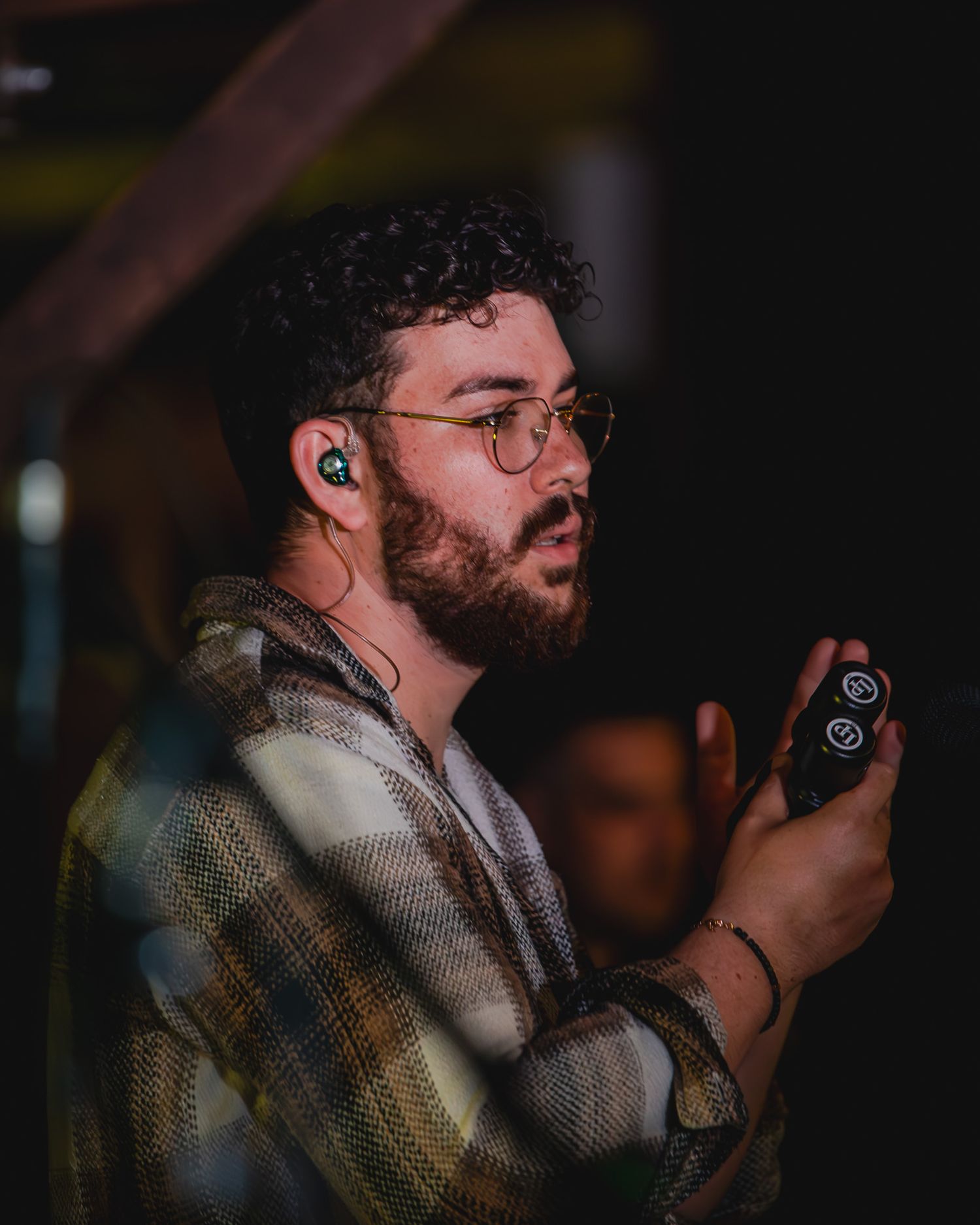 Young bearded man with curly hair and glasses holding a sound controller at a live event.