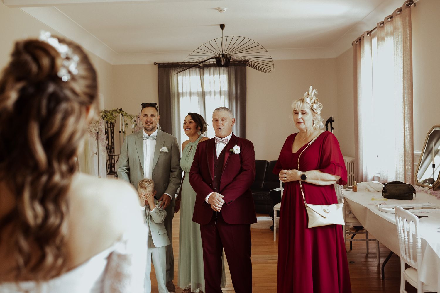 Bride being seen for the first time by family in elegant wedding attire during a pre-ceremony gathering indoors.