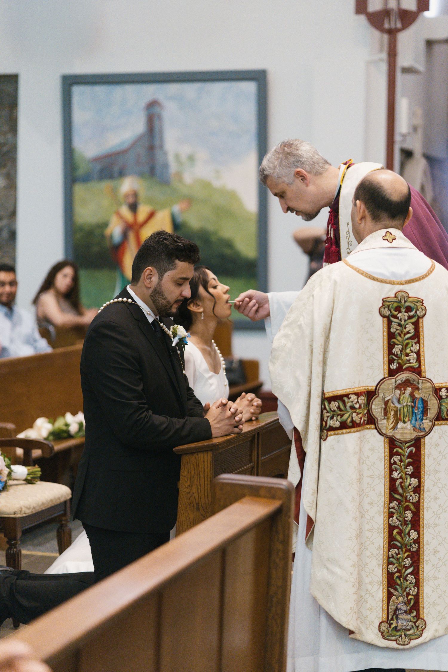 A couple exchanges vows during a church wedding ceremony as a priest in white vestments officiates.