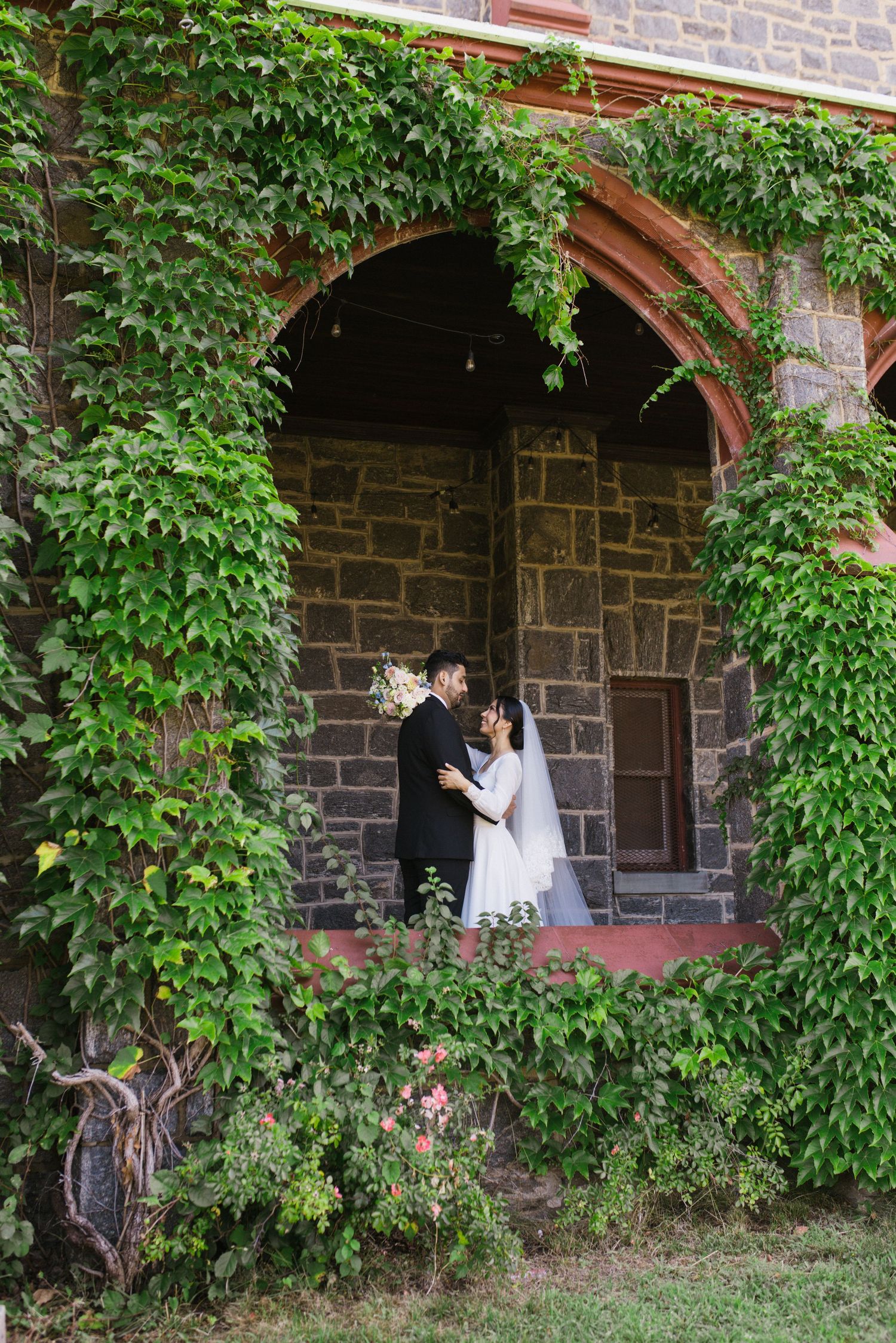 Bride and groom sharing romantic kiss framed by ivy-covered stone church archway.