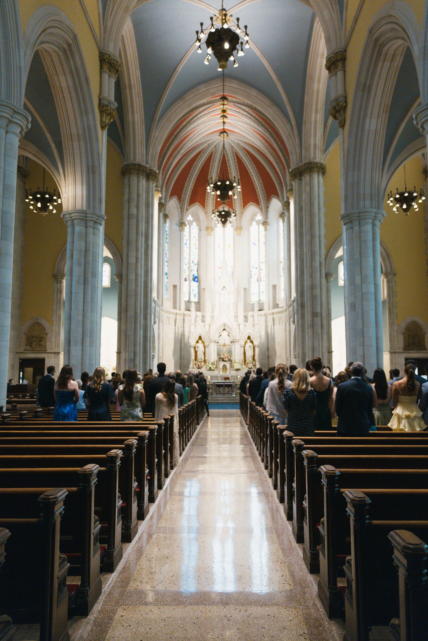 Elegant church wedding ceremony with guests seated in wooden pews along a marble aisle leading to an ornate altar.