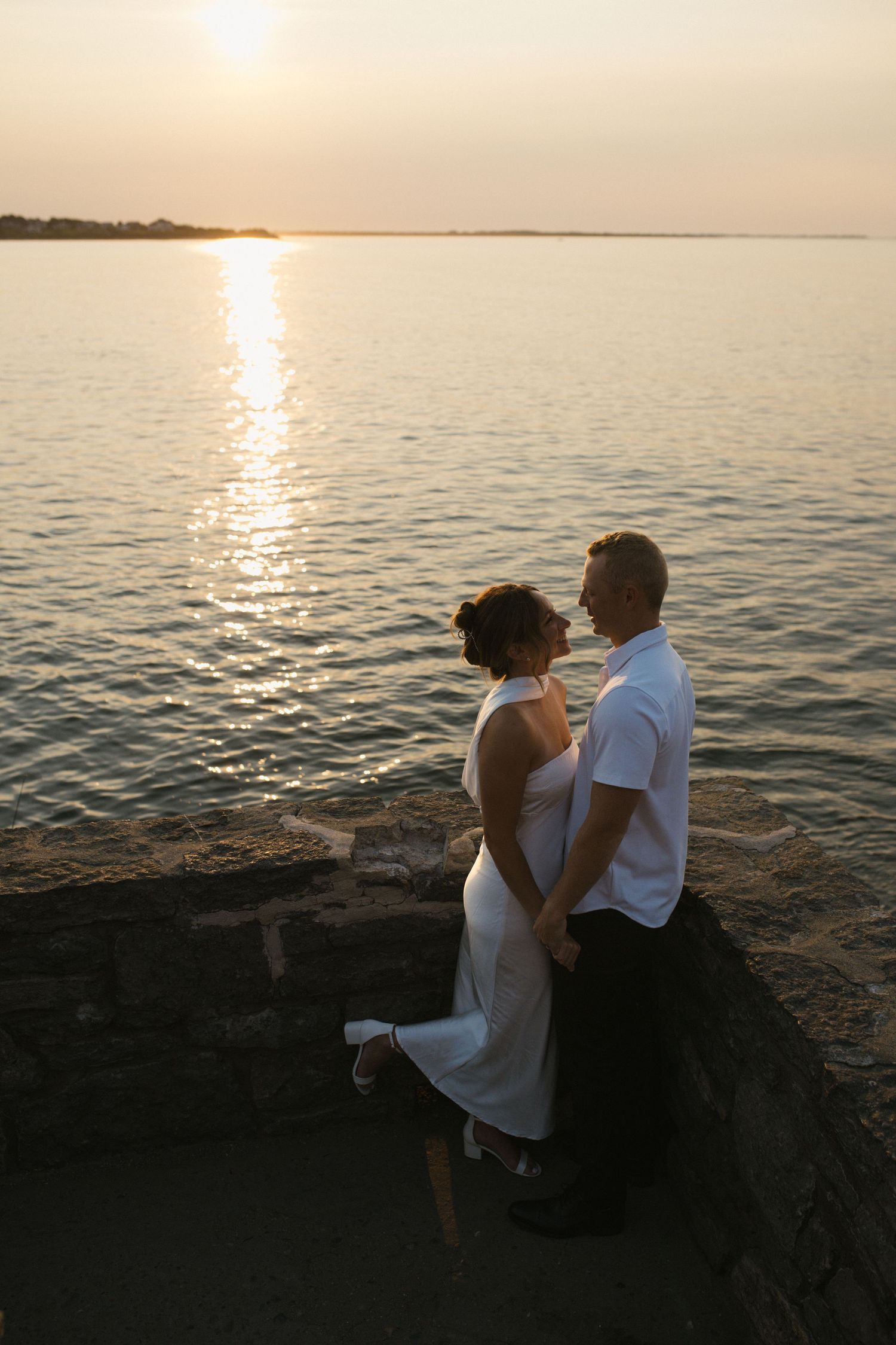 Couple sitting together on a stone ledge sharing a tender moment at golden sunset.