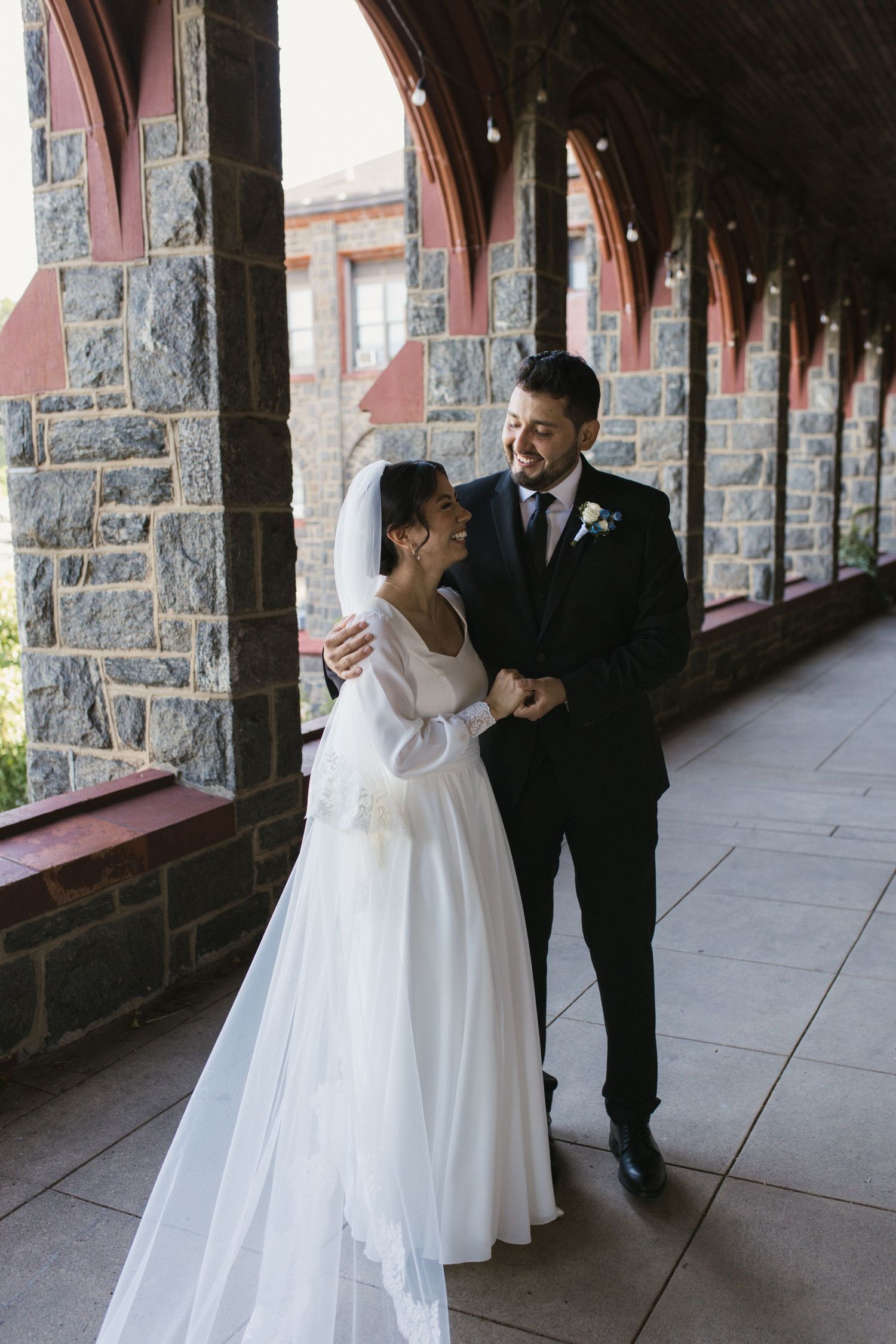 Bride and groom share a tender moment in a stone archway corridor on their wedding day.