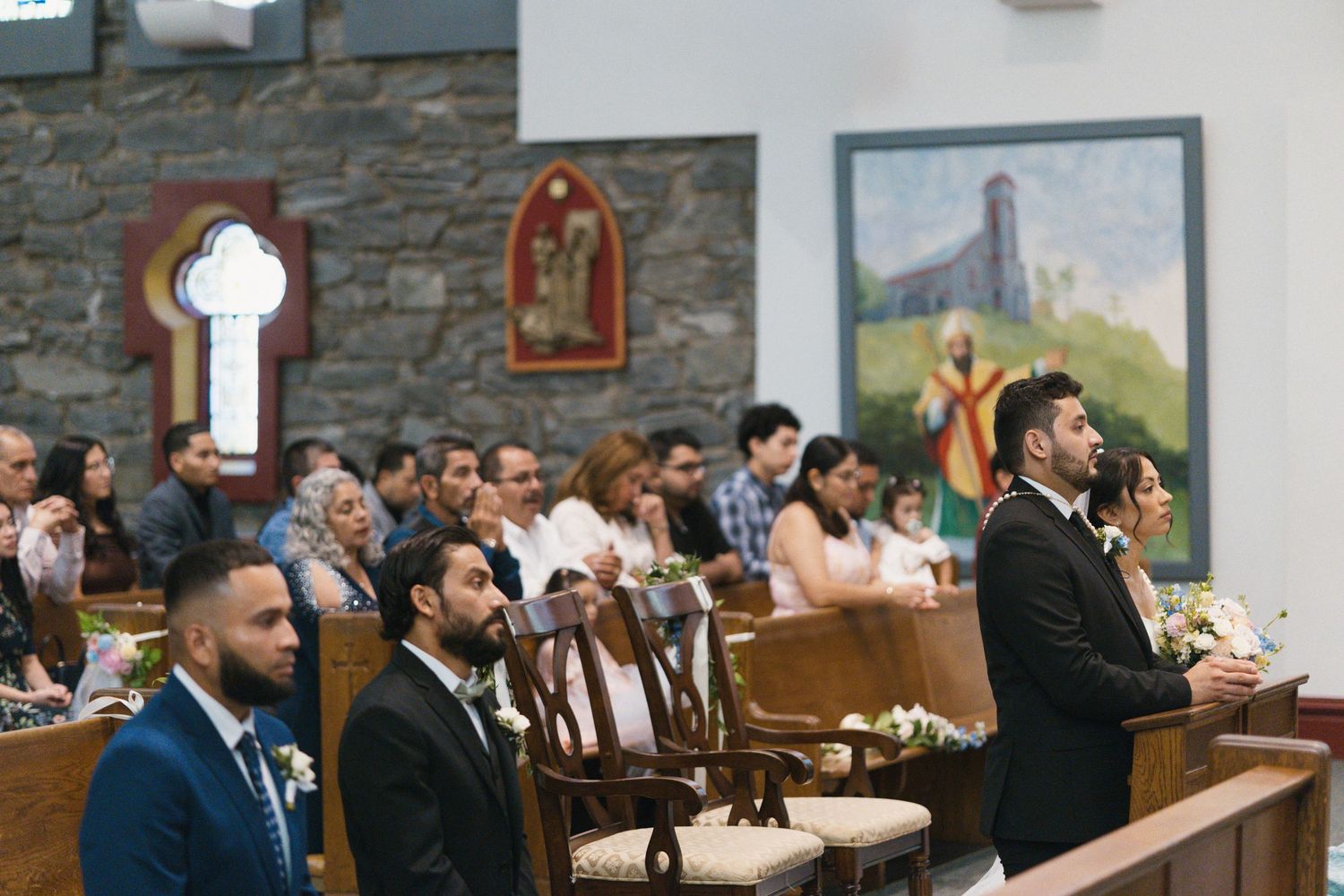Groom and groomsmen seated in church pews awaiting the bride during wedding ceremony.