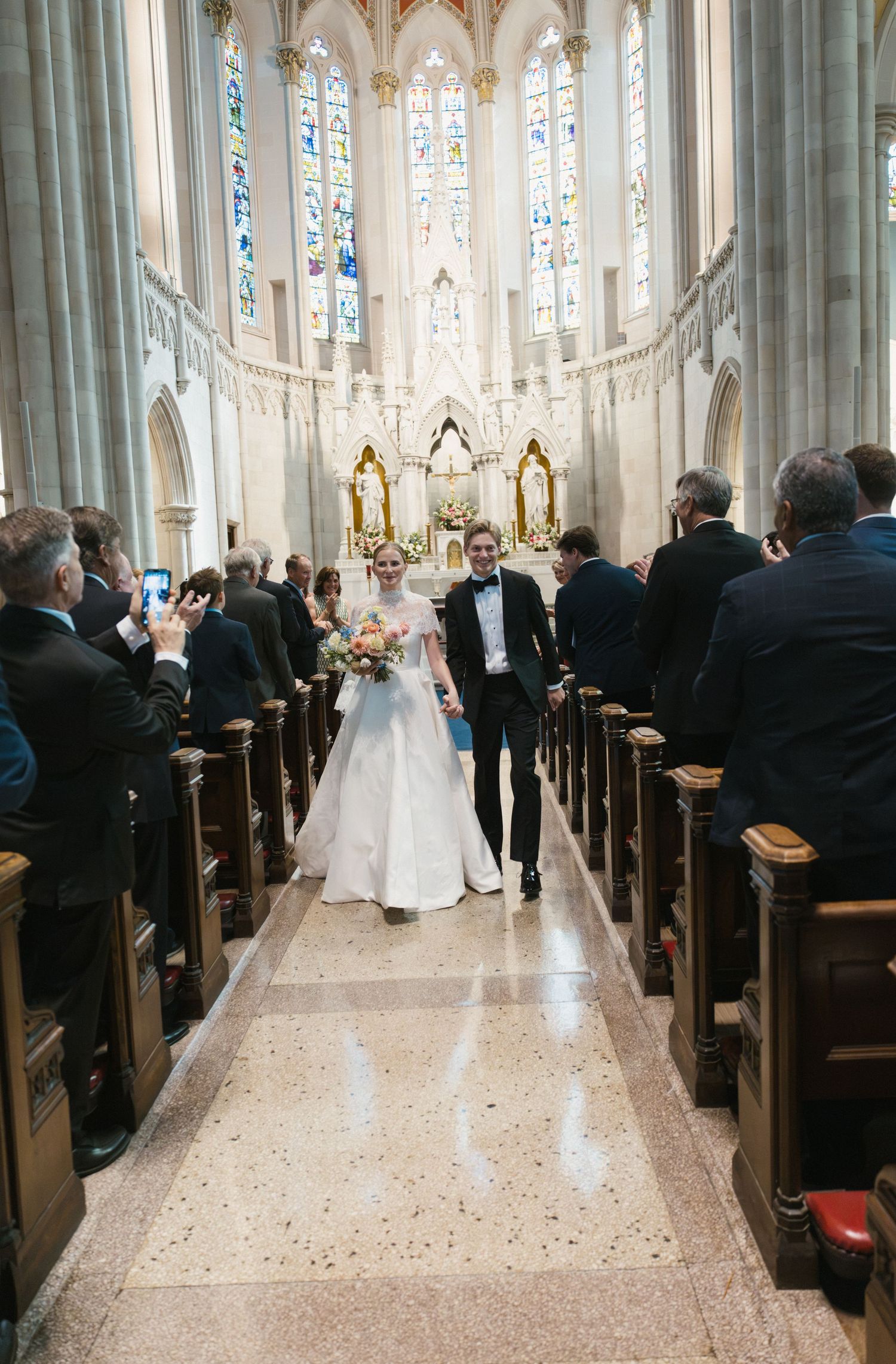 Newlyweds walking down the aisle of a grand cathedral church after their wedding ceremony.