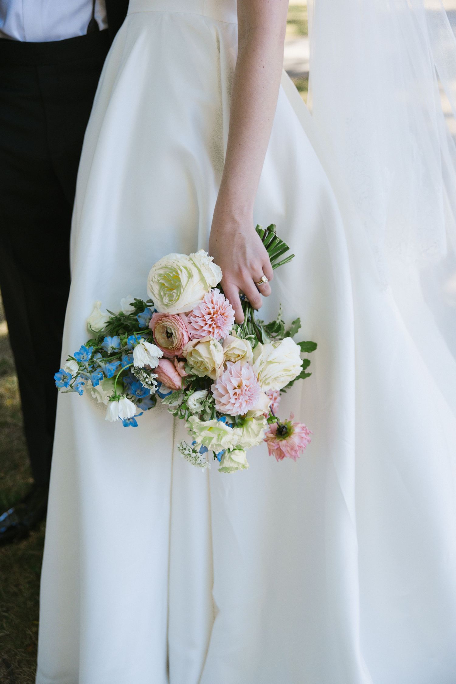 Bride holding a pastel wedding bouquet of pink, white, and blue flowers against her white ball gown.